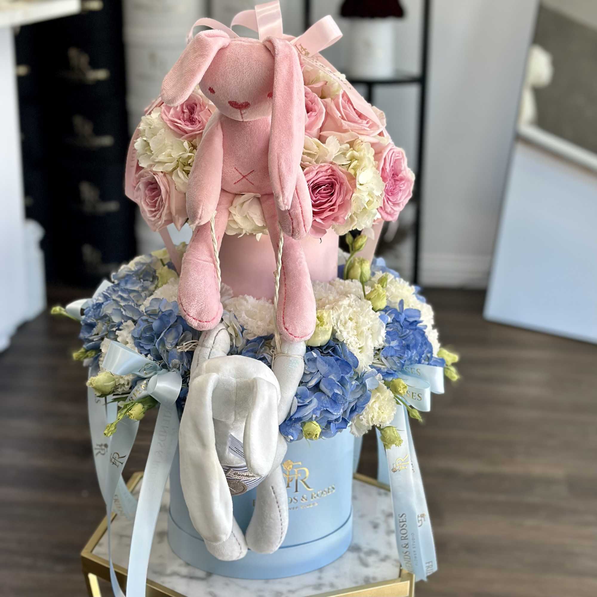 Pink plush bunny sitting on a box of pink and blue flowers