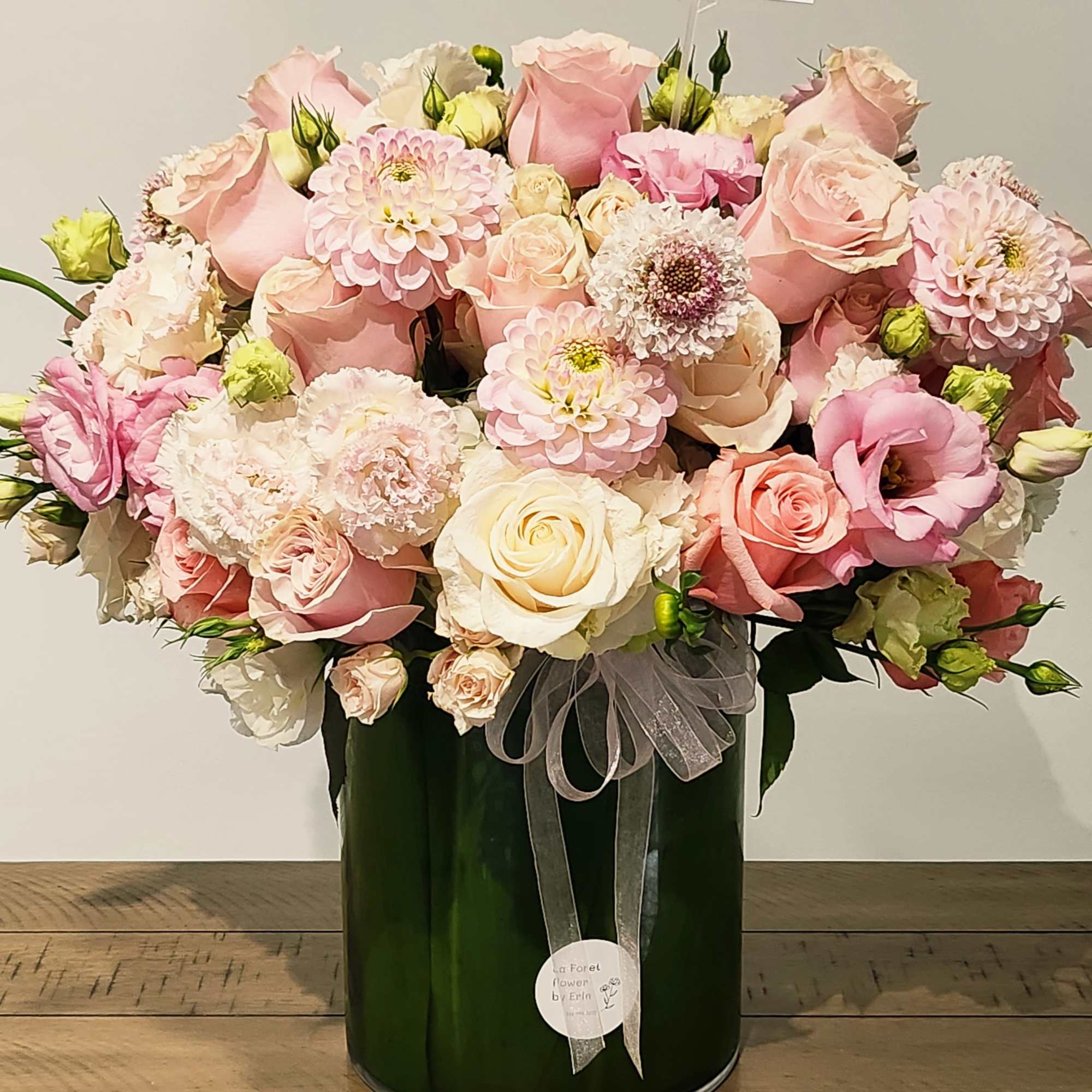 Pink and cream rose bouquet in a dark green vase with a sheer ribbon