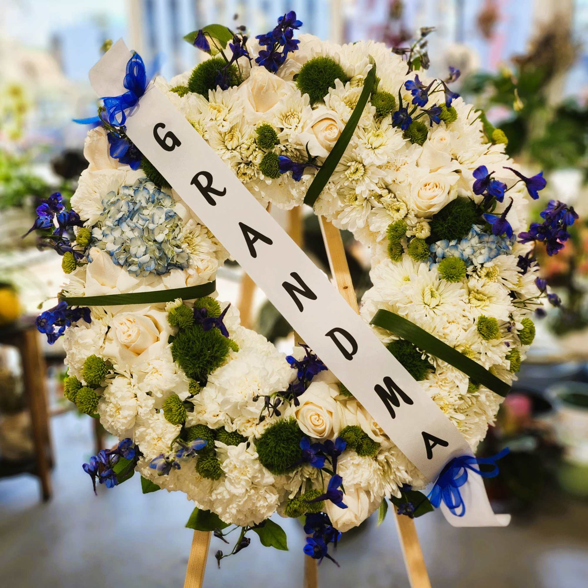 White floral wreath with blue ribbon and a diagonal memorial sash