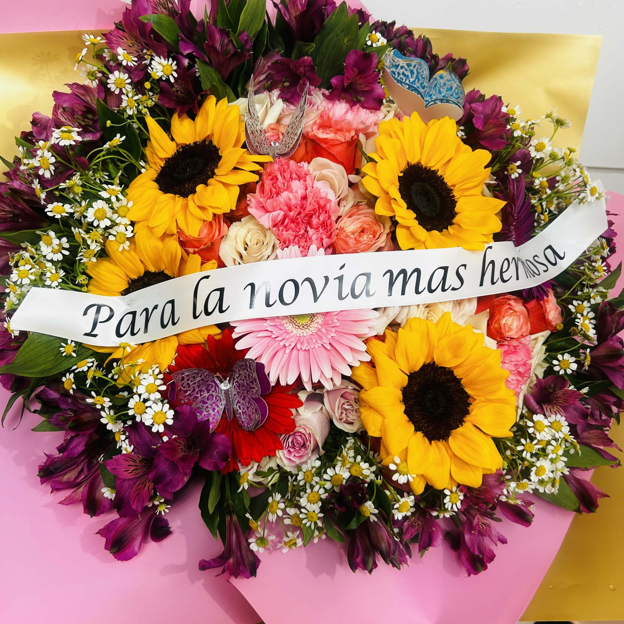 Mixed bouquet with sunflowers, pink roses, and purple flowers with a ribbon