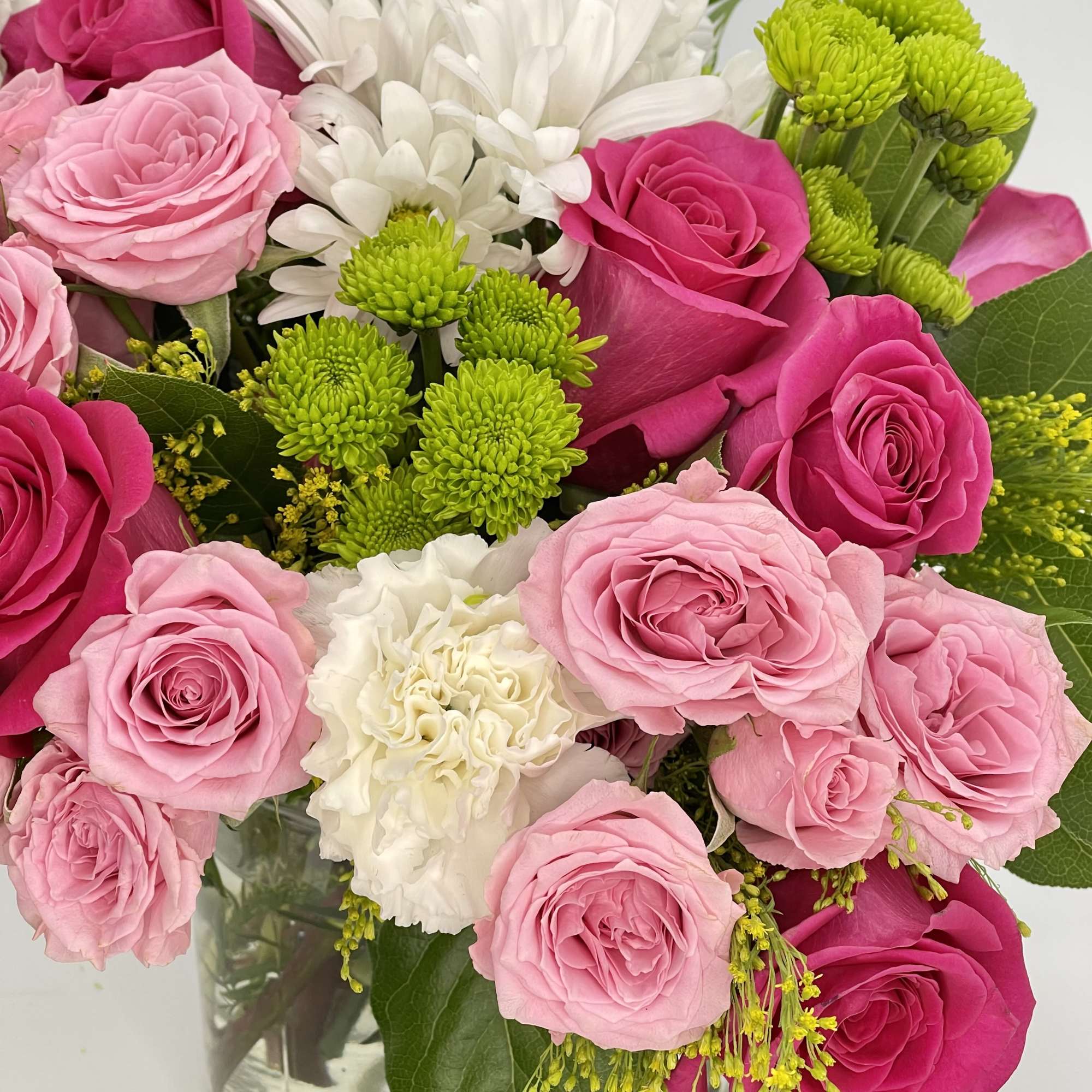 Pink roses, white mums, and green button poms arranged in a clear glass vase