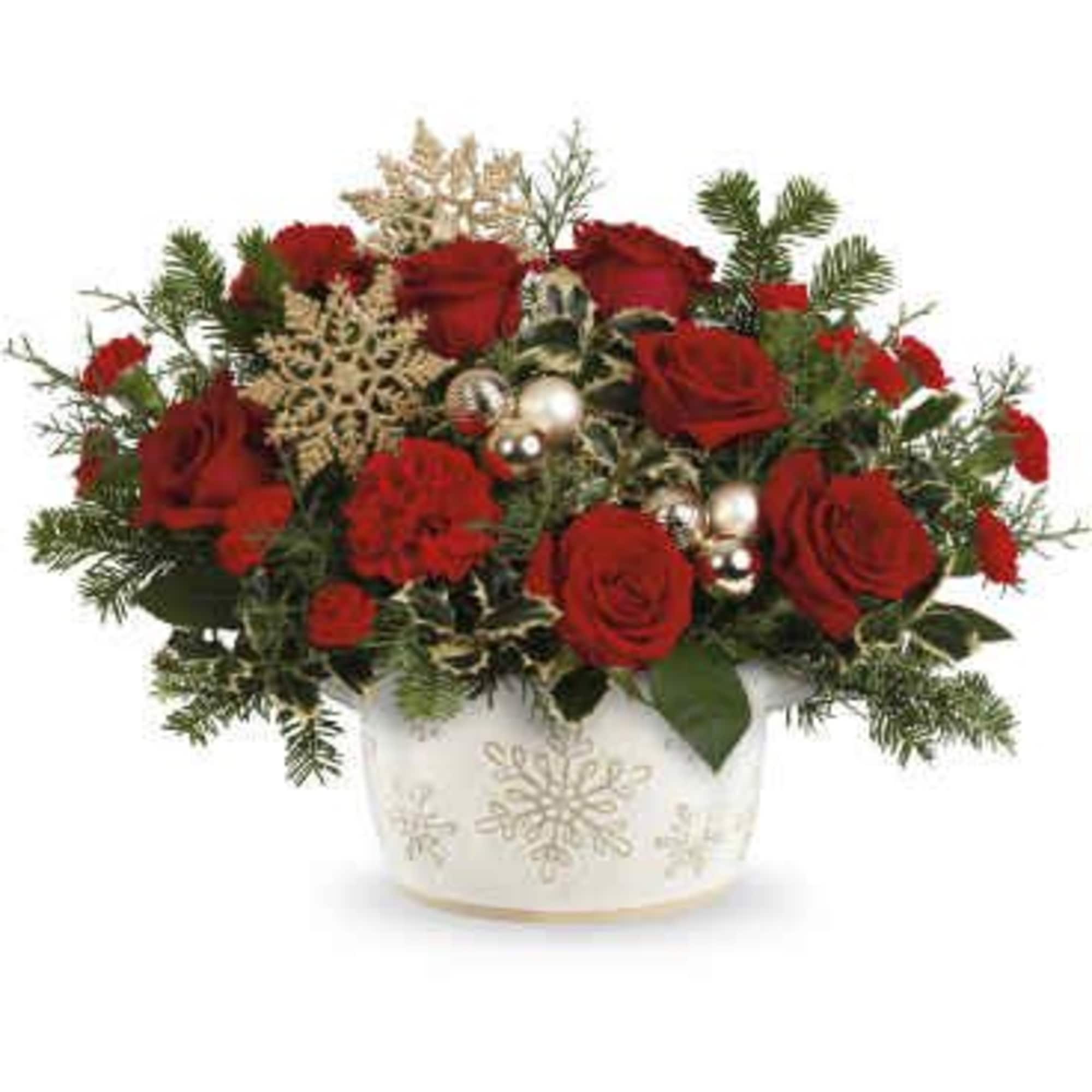 Red roses arranged in a white snowflake vase with holiday accents