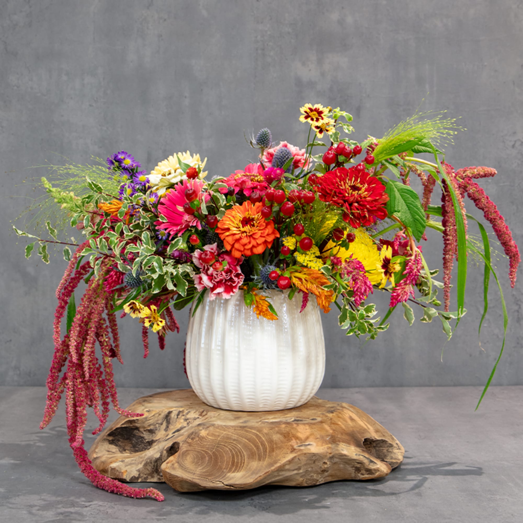 Colorful mixed flower arrangement in a white vase on a wooden base