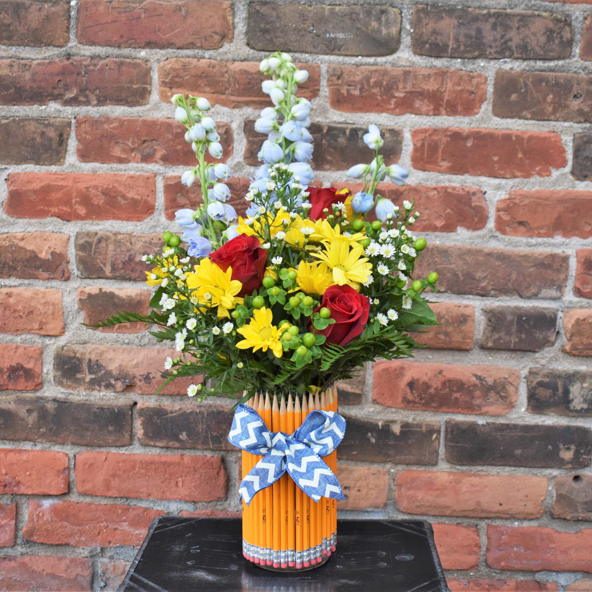 This colorful array of yellow daisies, red roses, asters, hypericum berries, blue