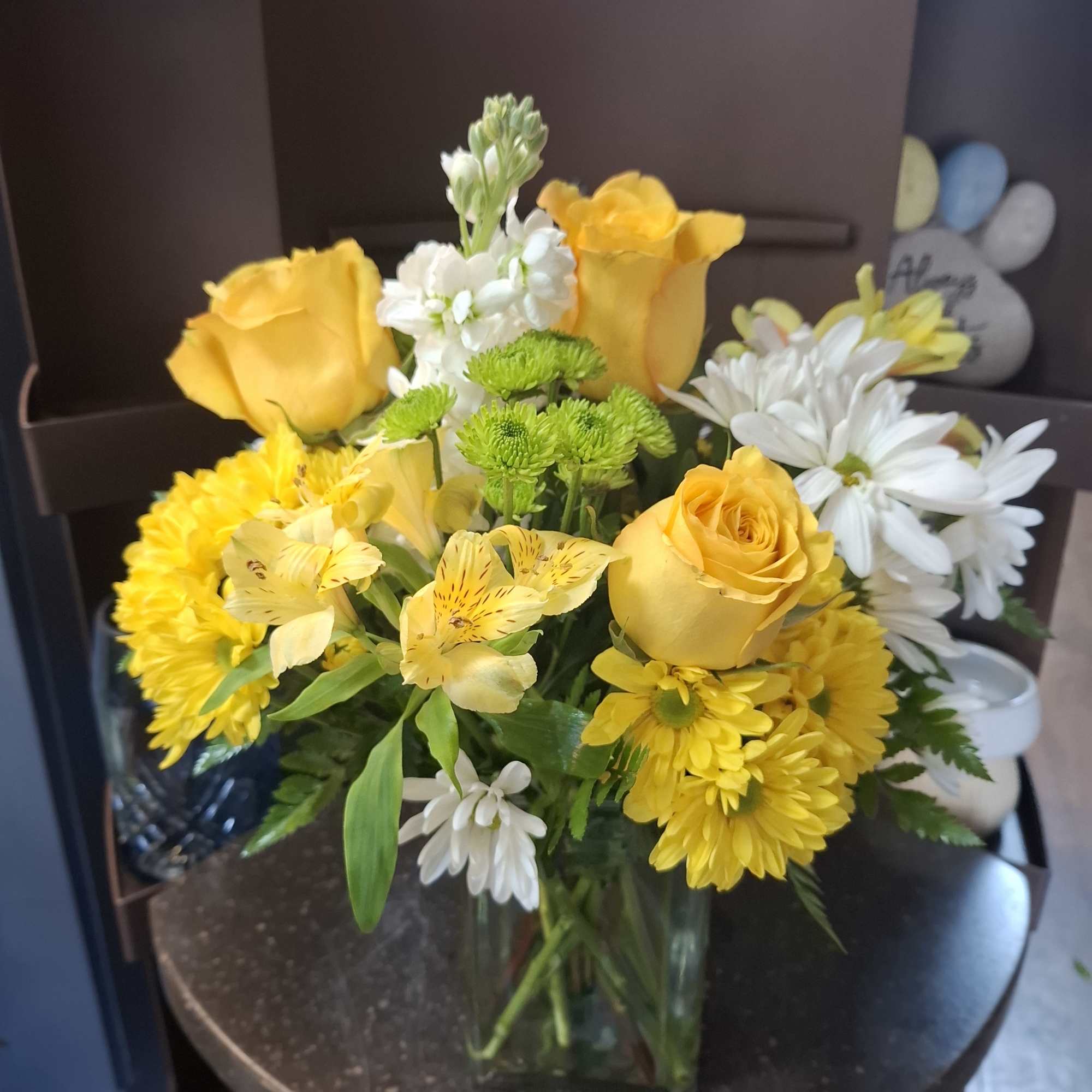 Yellow roses and white daisies arranged in a clear glass vase