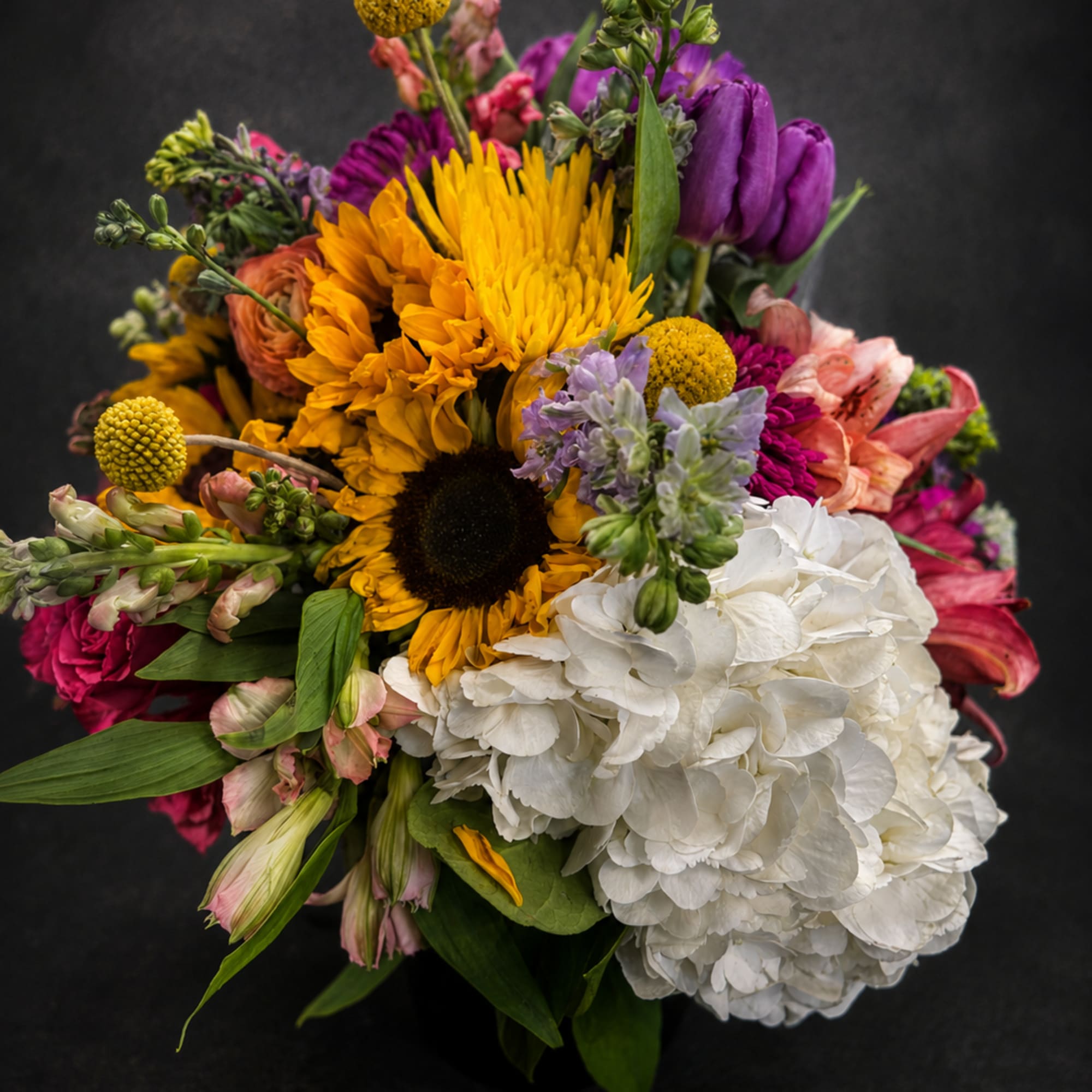 A lower arrangement using sunflowers and other bright flowers to make someone