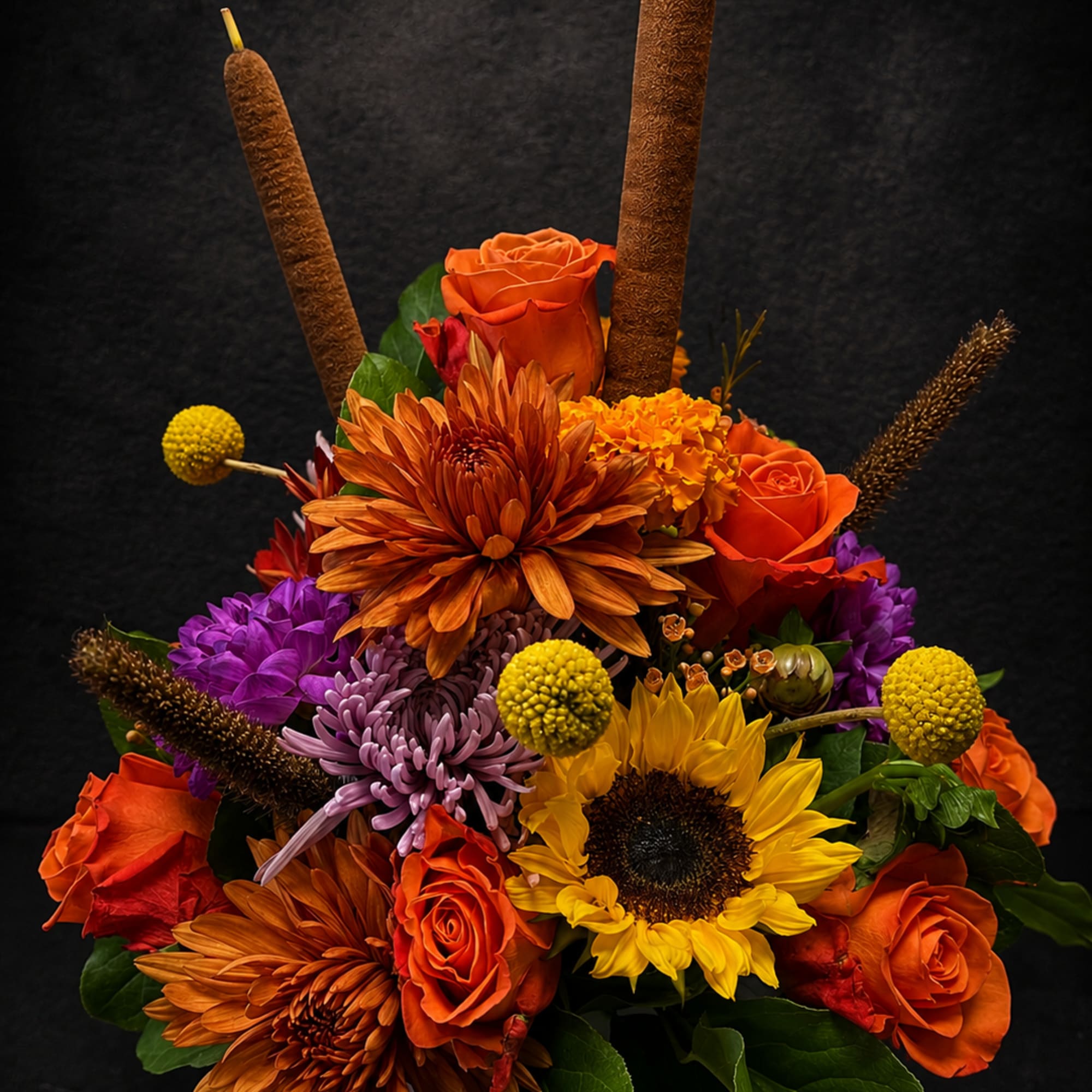 Bright, bold orange roses and a single sunny sunflower anchor this flower