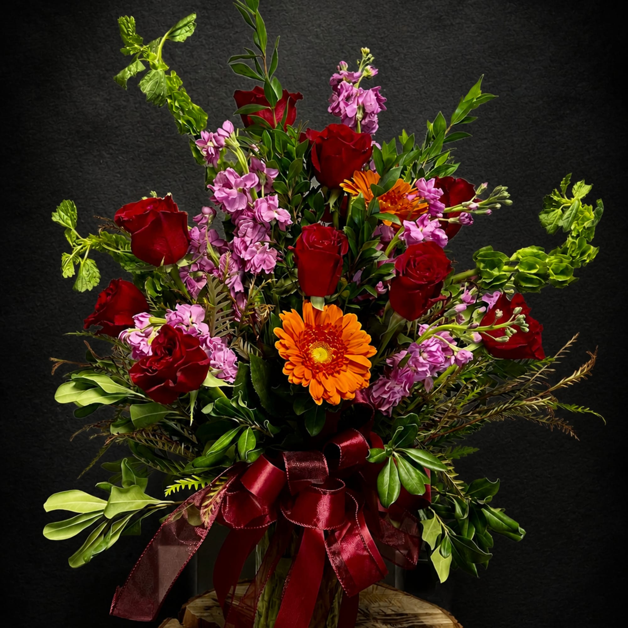 Deep, velvety red roses pair with bright orange gerbera daisies and soft