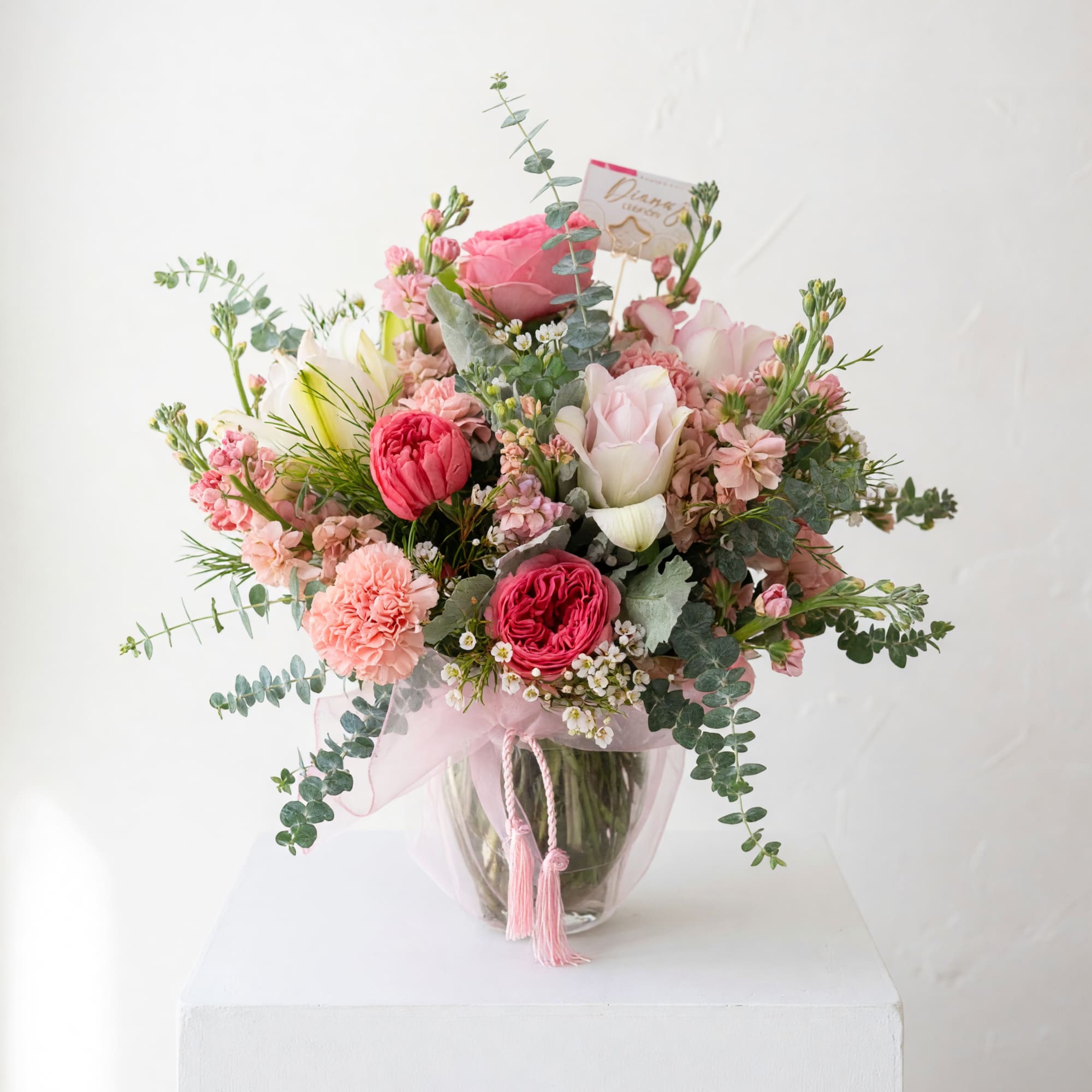 Pink and white mixed bouquet in a clear glass vase with a pink ribbon