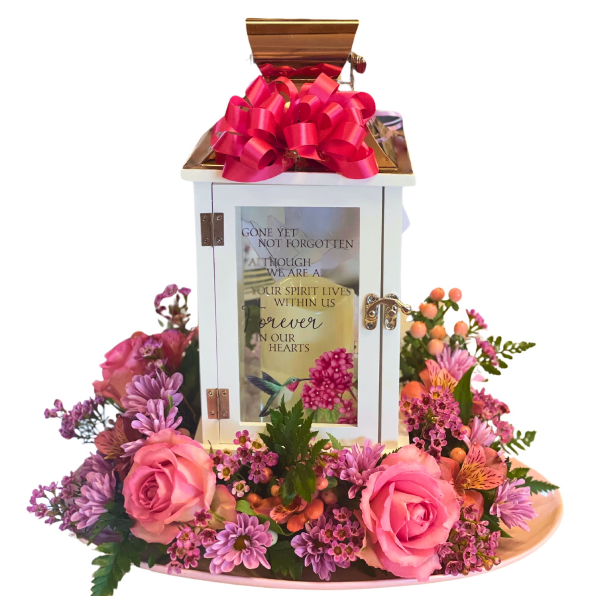 Pink roses and purple flowers arranged around a white memorial lantern with a red bow.