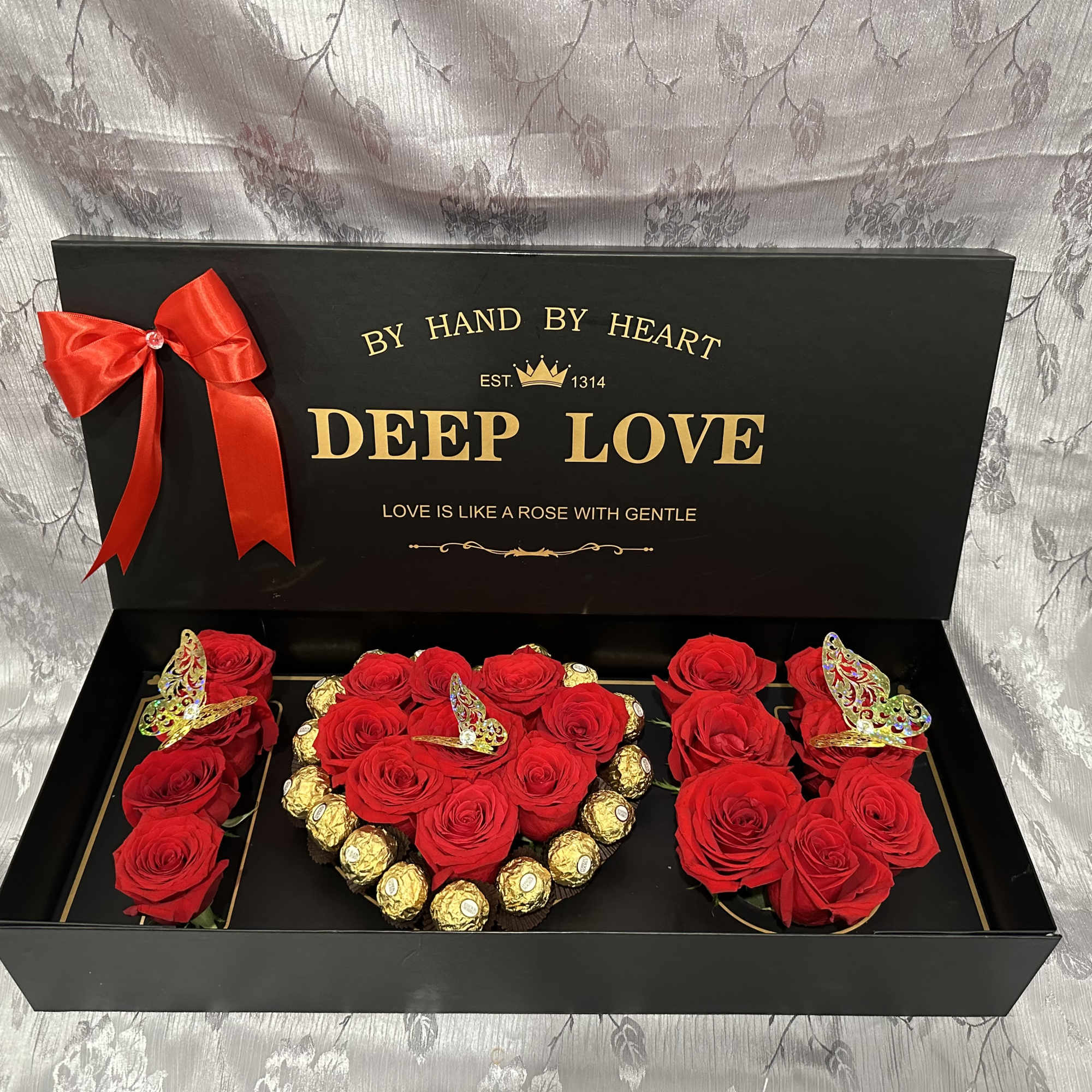 Black gift box with red roses, gold chocolates, and a red ribbon
