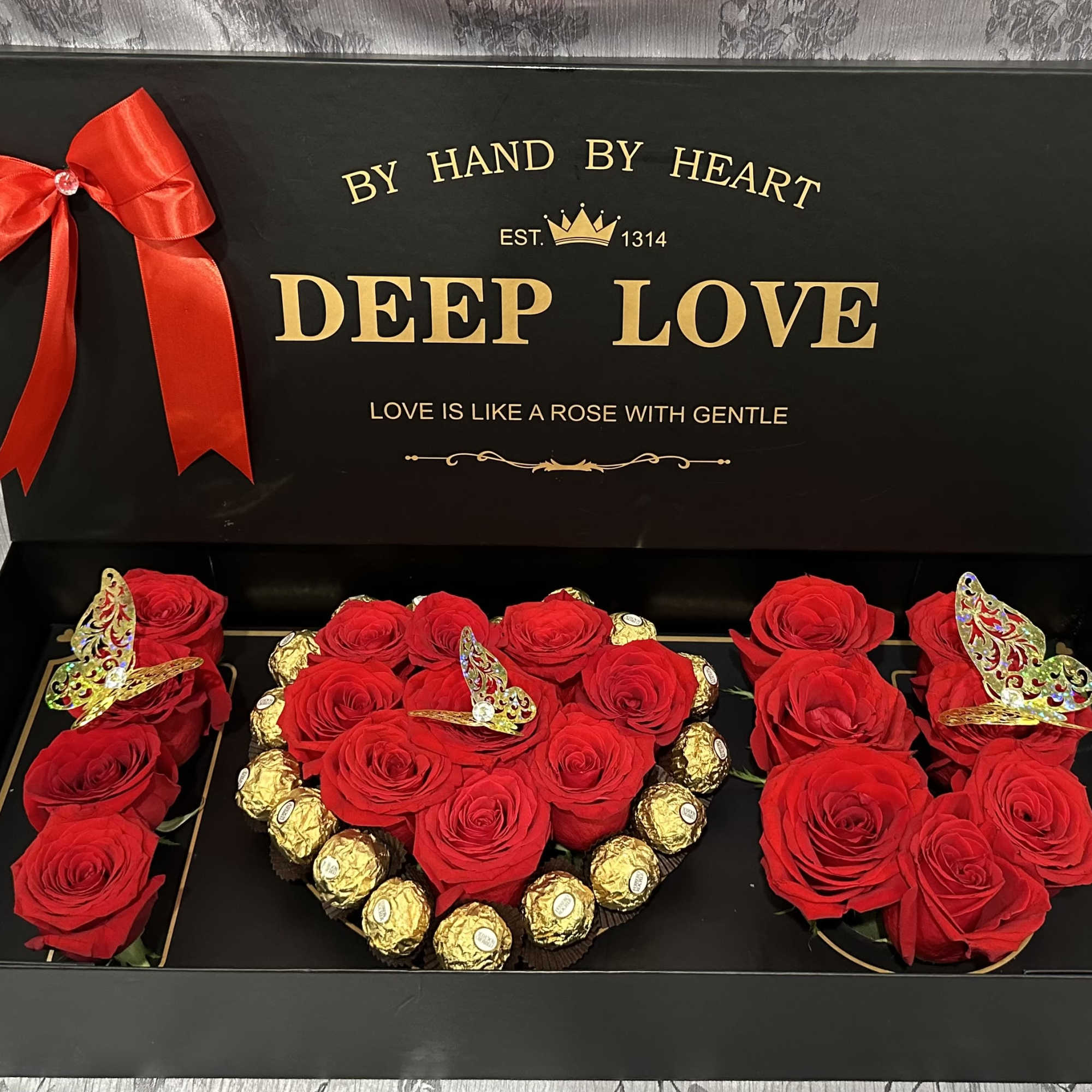 Red roses arranged in a black gift box with Ferrero Rocher chocolates and butterfly decorations.