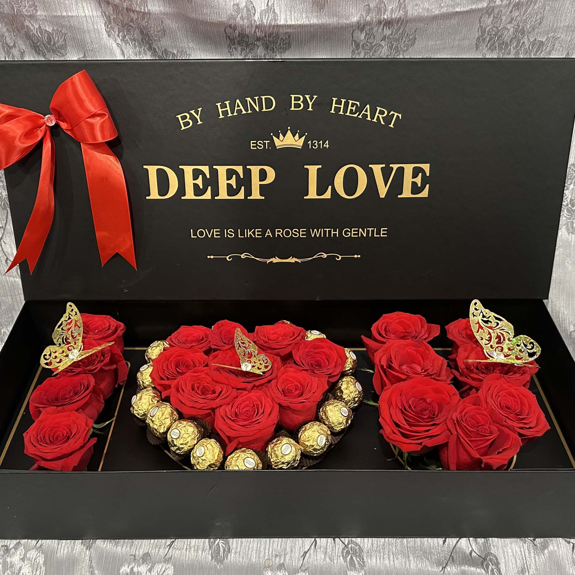 Red roses and chocolates arranged in a black gift box with a ribbon.