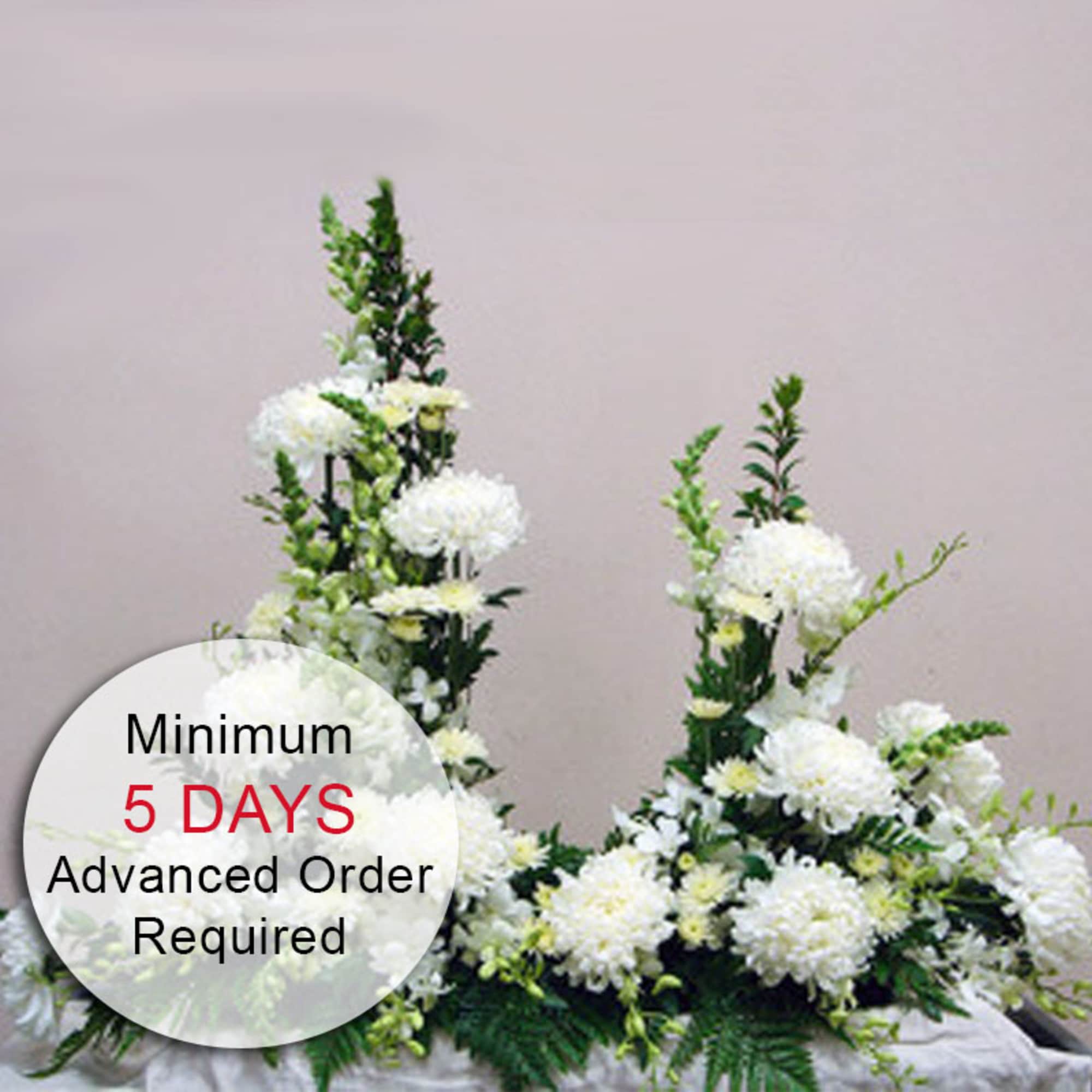 Tall white floral sympathy arrangement with clustered mums and vertical accents on a draped surface