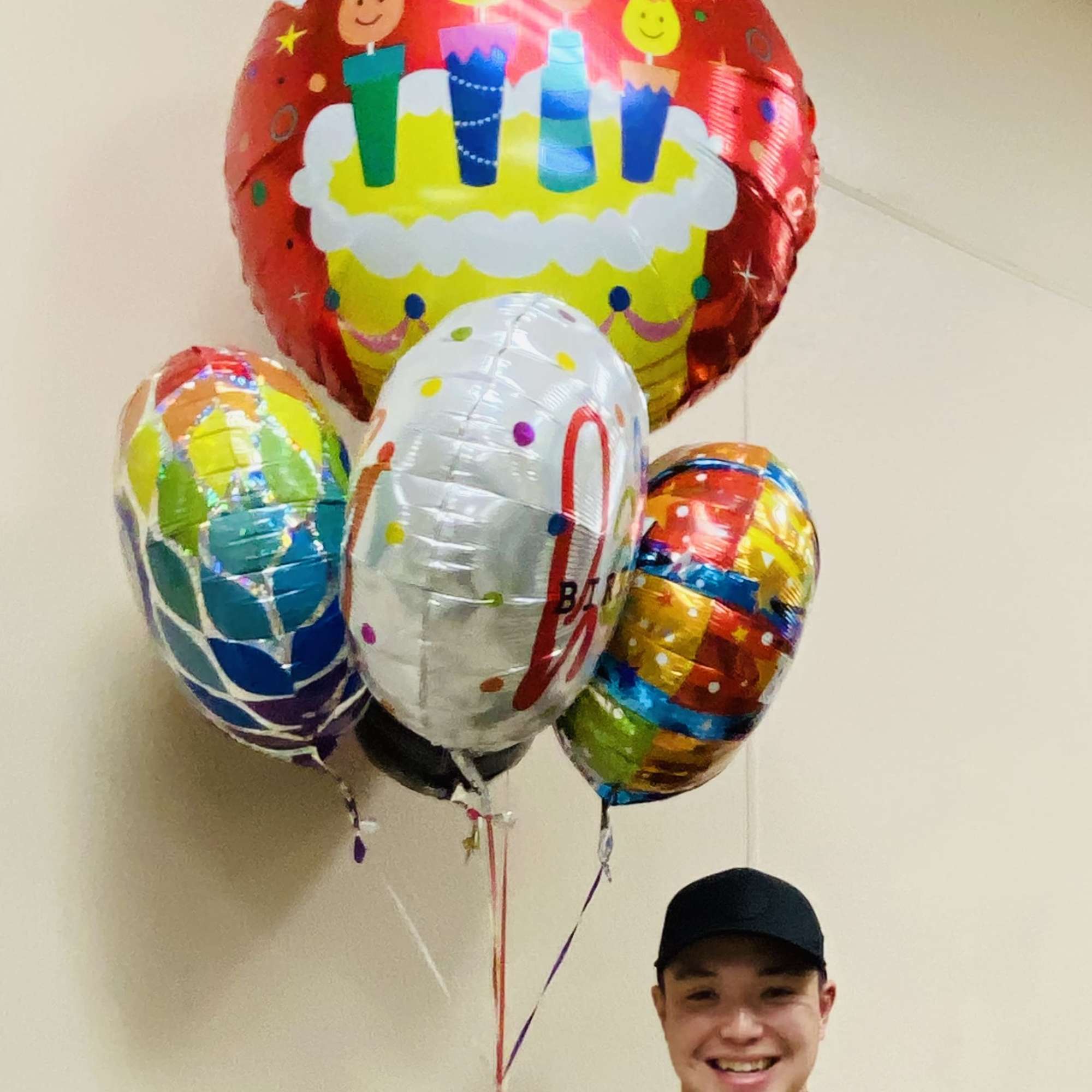 Bundle of colorful birthday mylar balloons held by a smiling person