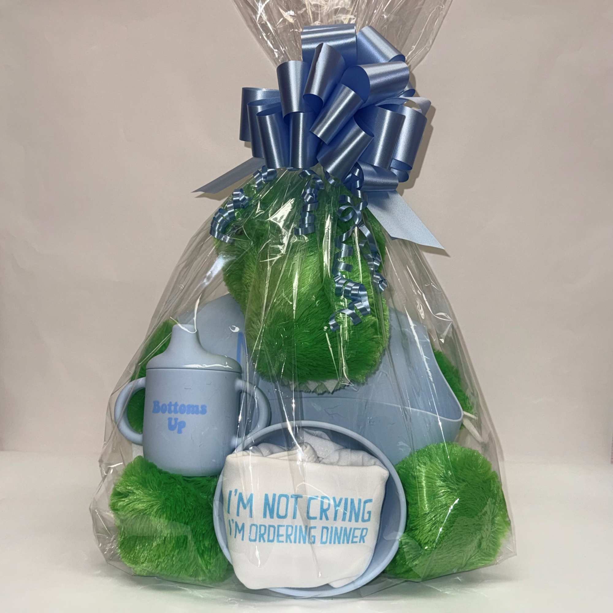 Baby-themed blue and green gift set in cellophane with bow, sippy cup, bib, and plush items