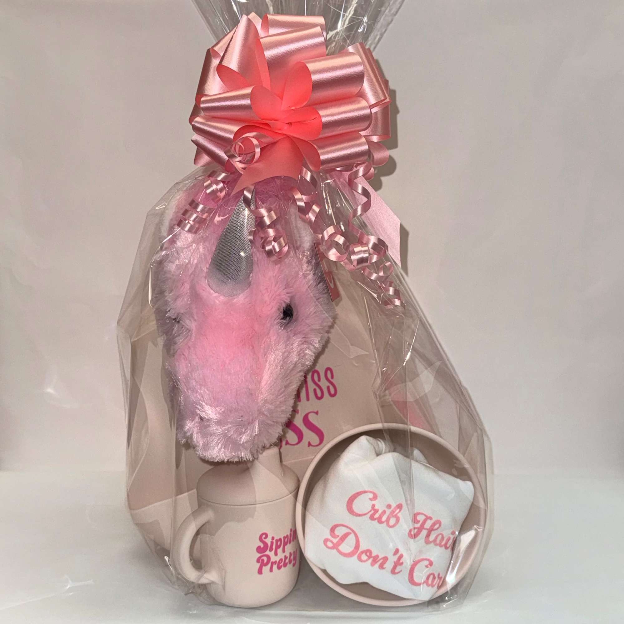 Baby gift set with pink plush unicorn, mug, and cloth wrapped in cellophane with a pink bow