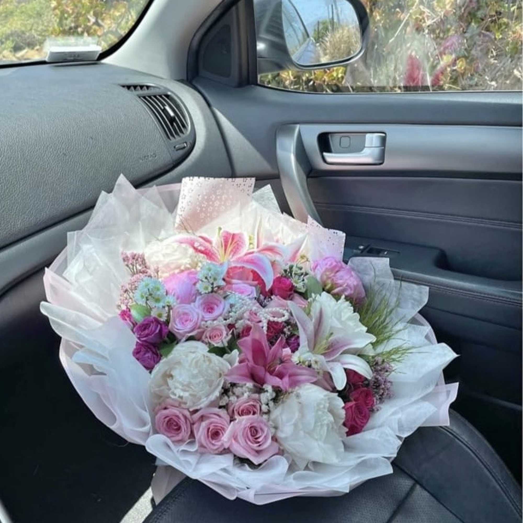 Pink and white mixed bouquet wrapped in tissue paper on a car seat