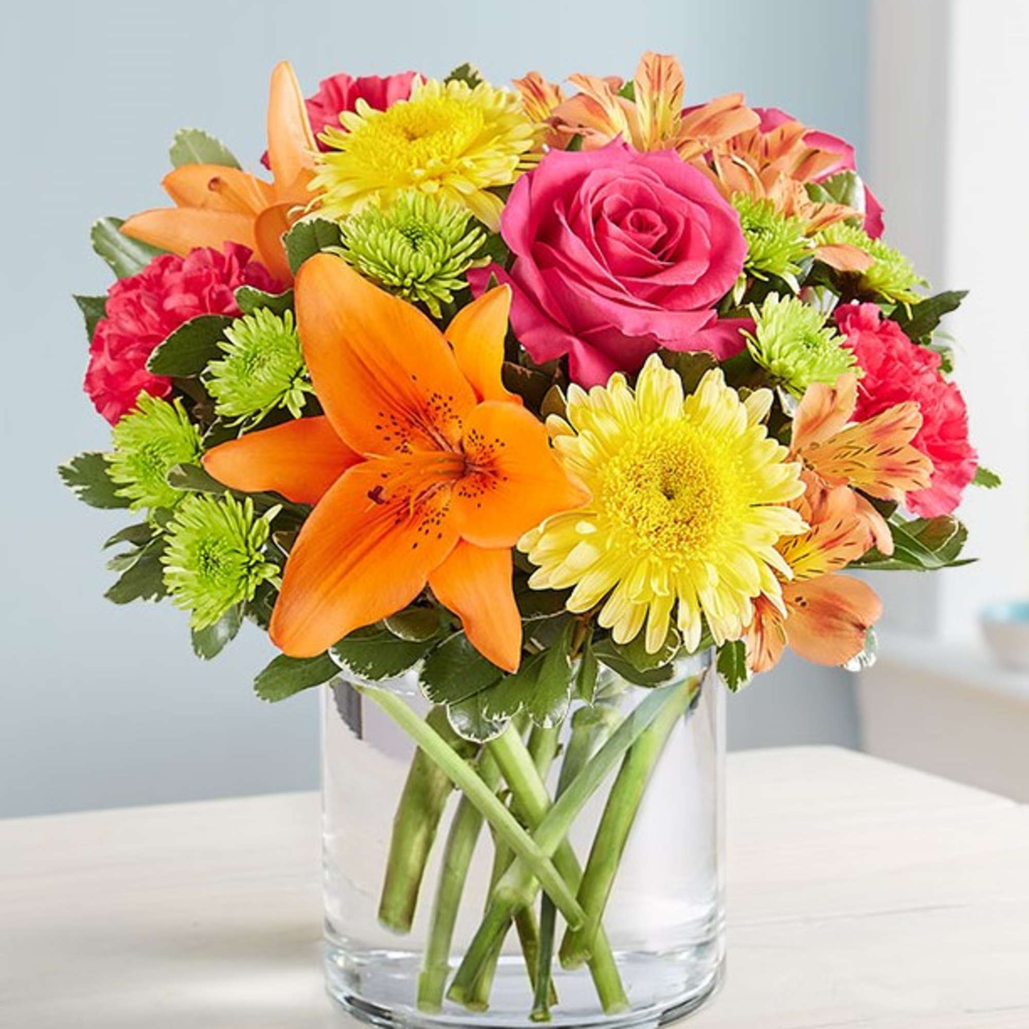 Mixed bouquet of roses, lilies, and chrysanthemums in a clear glass vase