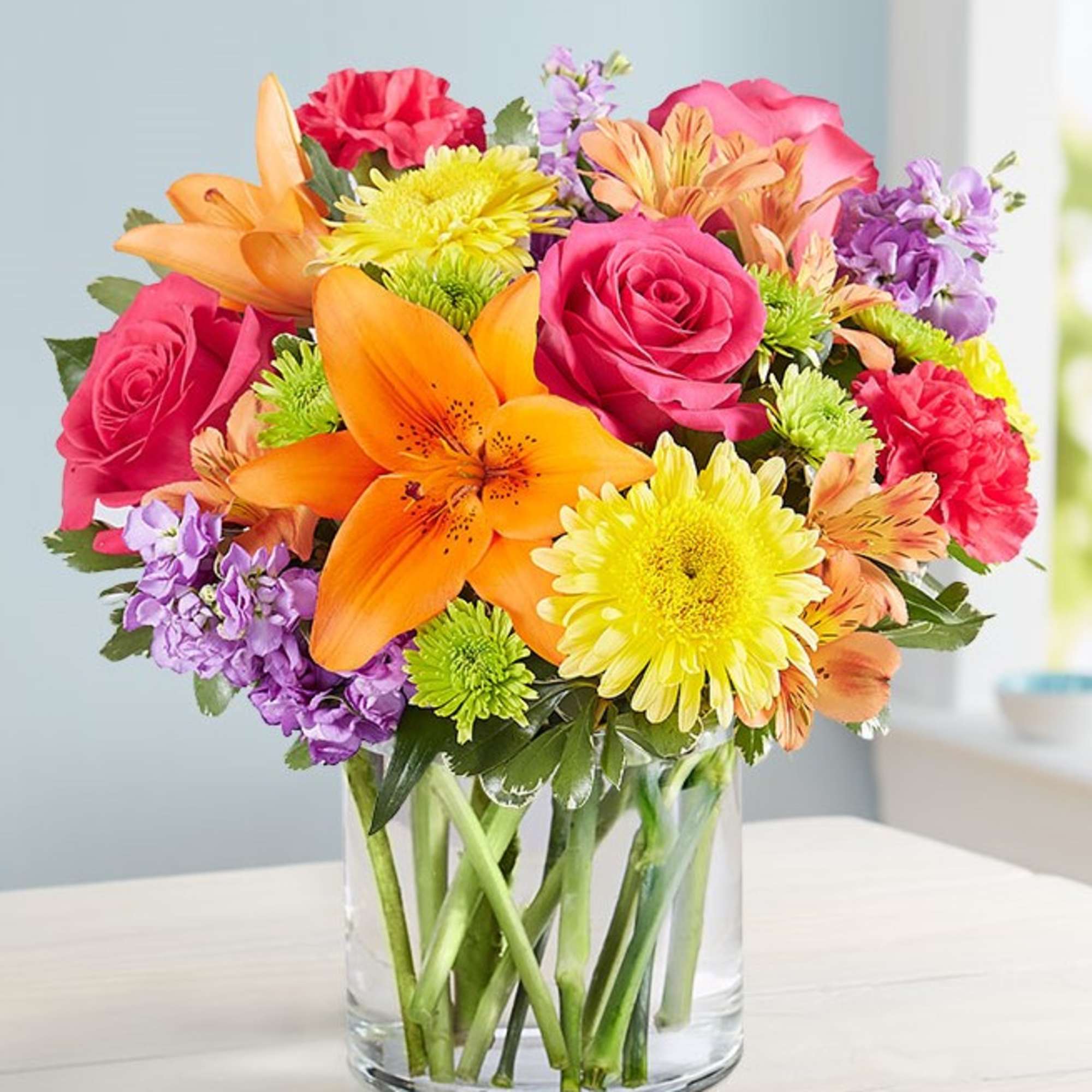 Mixed bouquet of roses, lilies, and daisies in a clear glass vase