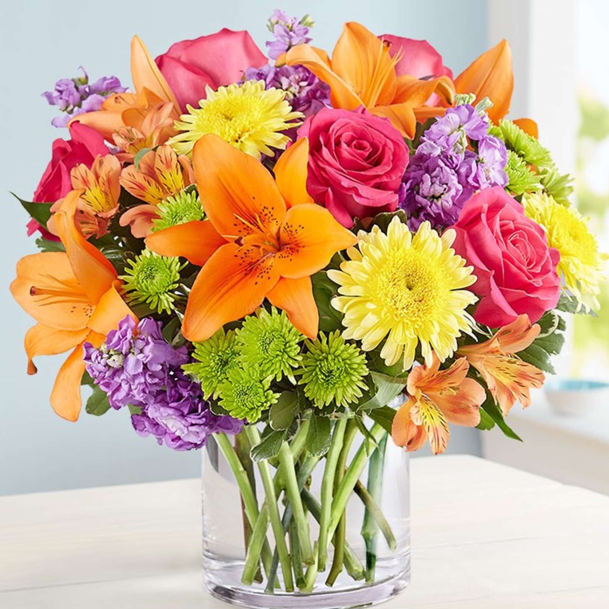 Mixed bouquet of orange lilies, pink roses, and purple flowers in a clear glass vase