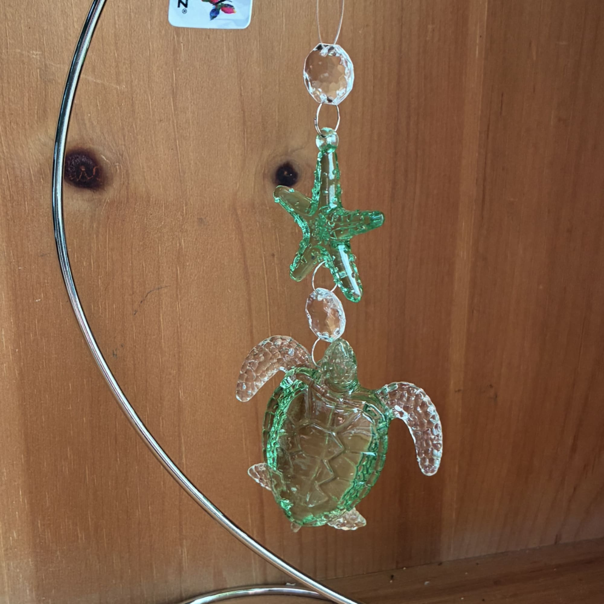 Green crystal turtle and starfish ornament hanging from a silver metal stand on a wooden background