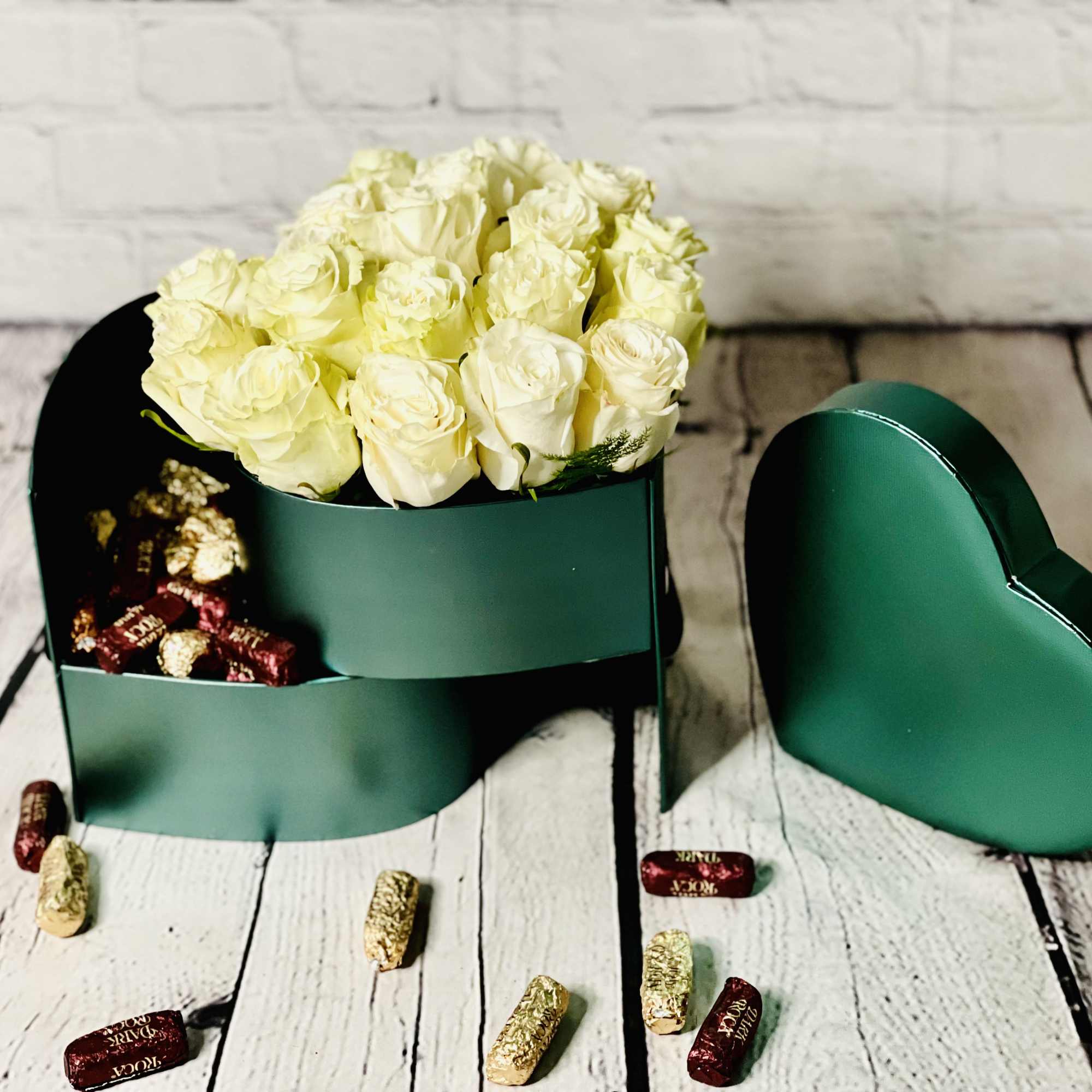 White roses in a green heart-shaped box with chocolates