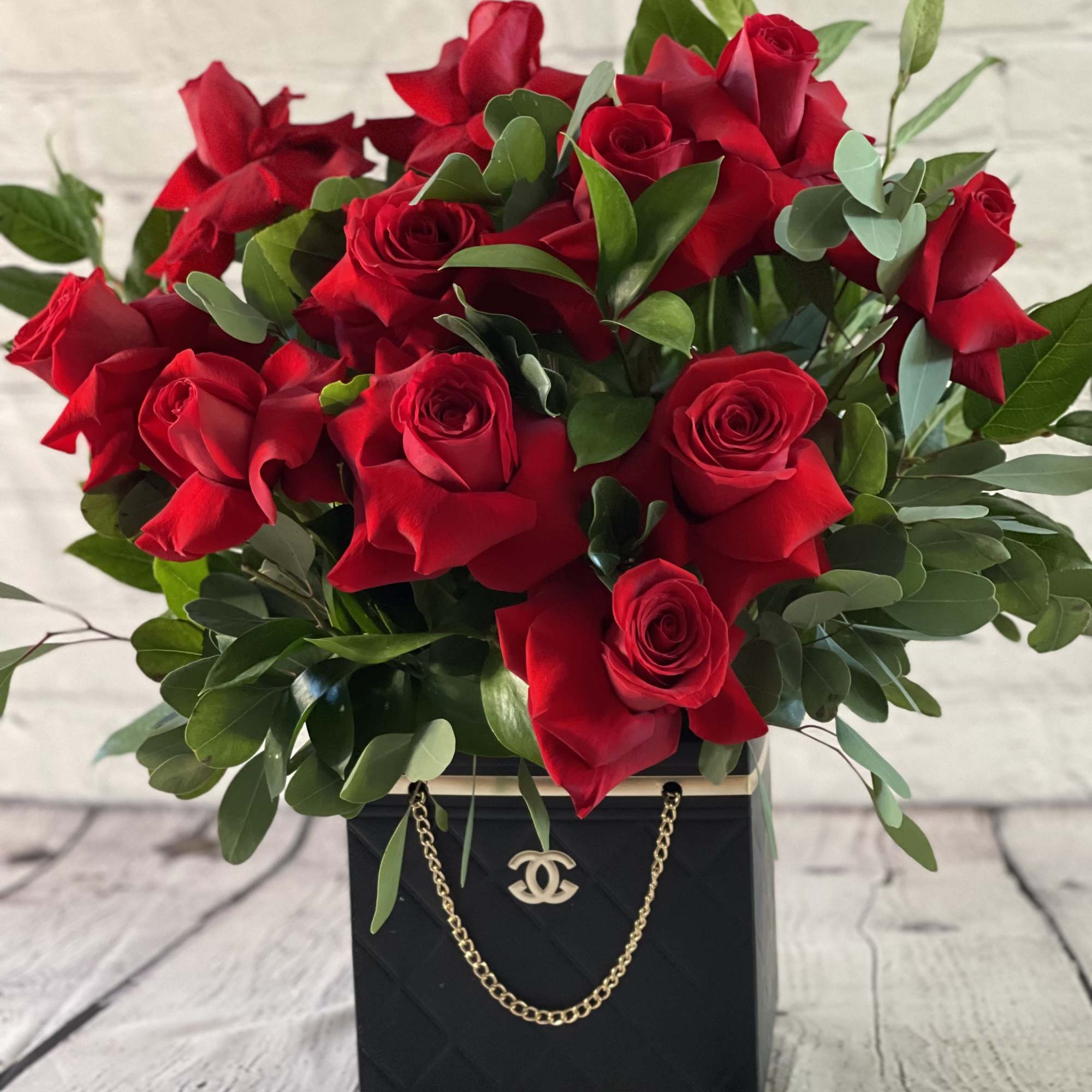 Red roses arranged in a black box with a gold chain handle
