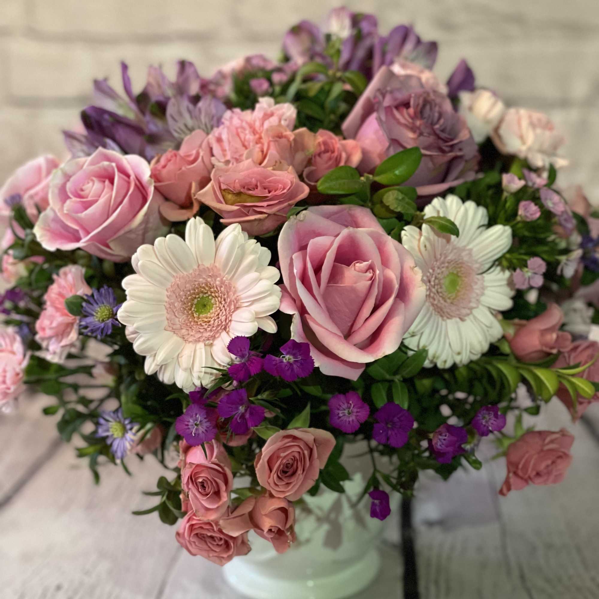 Pink and purple rose bouquet with white daisy-like blooms in a white vase