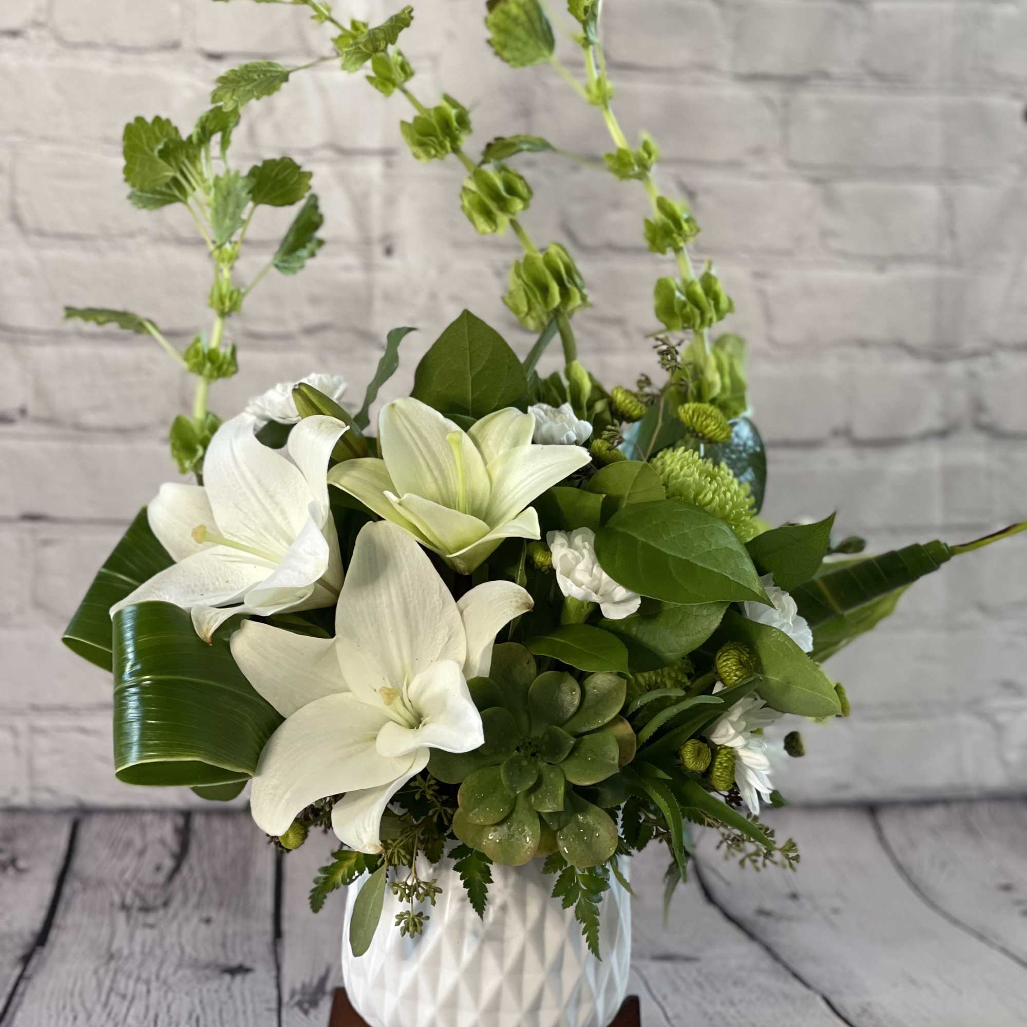 White lilies and green succulents arranged in a white vase