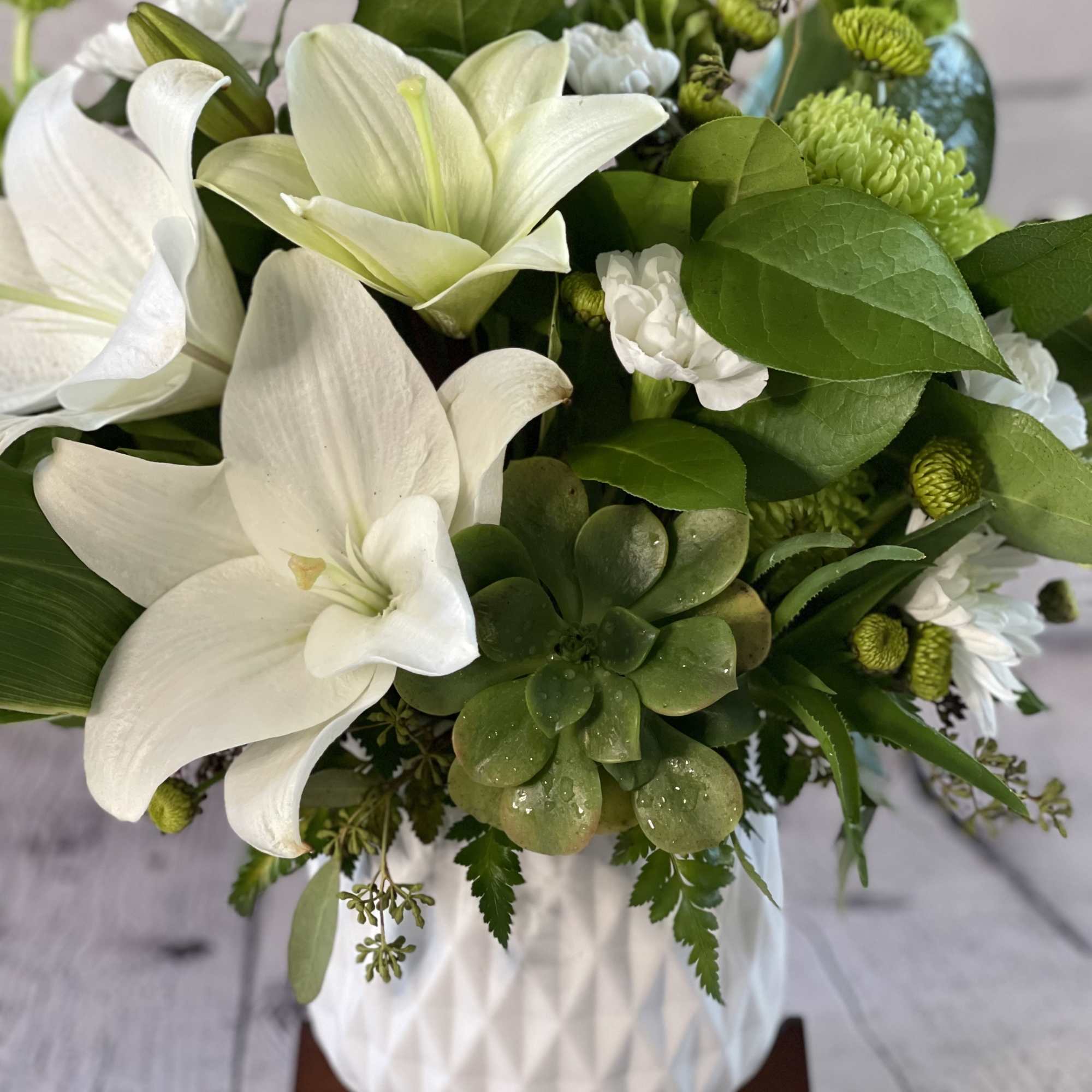 White lilies and green blooms arranged in a white vase