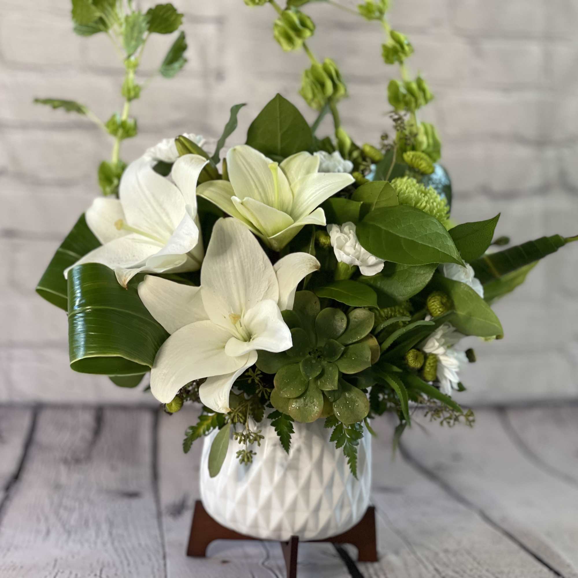 White lilies and green succulents in a white ceramic vase