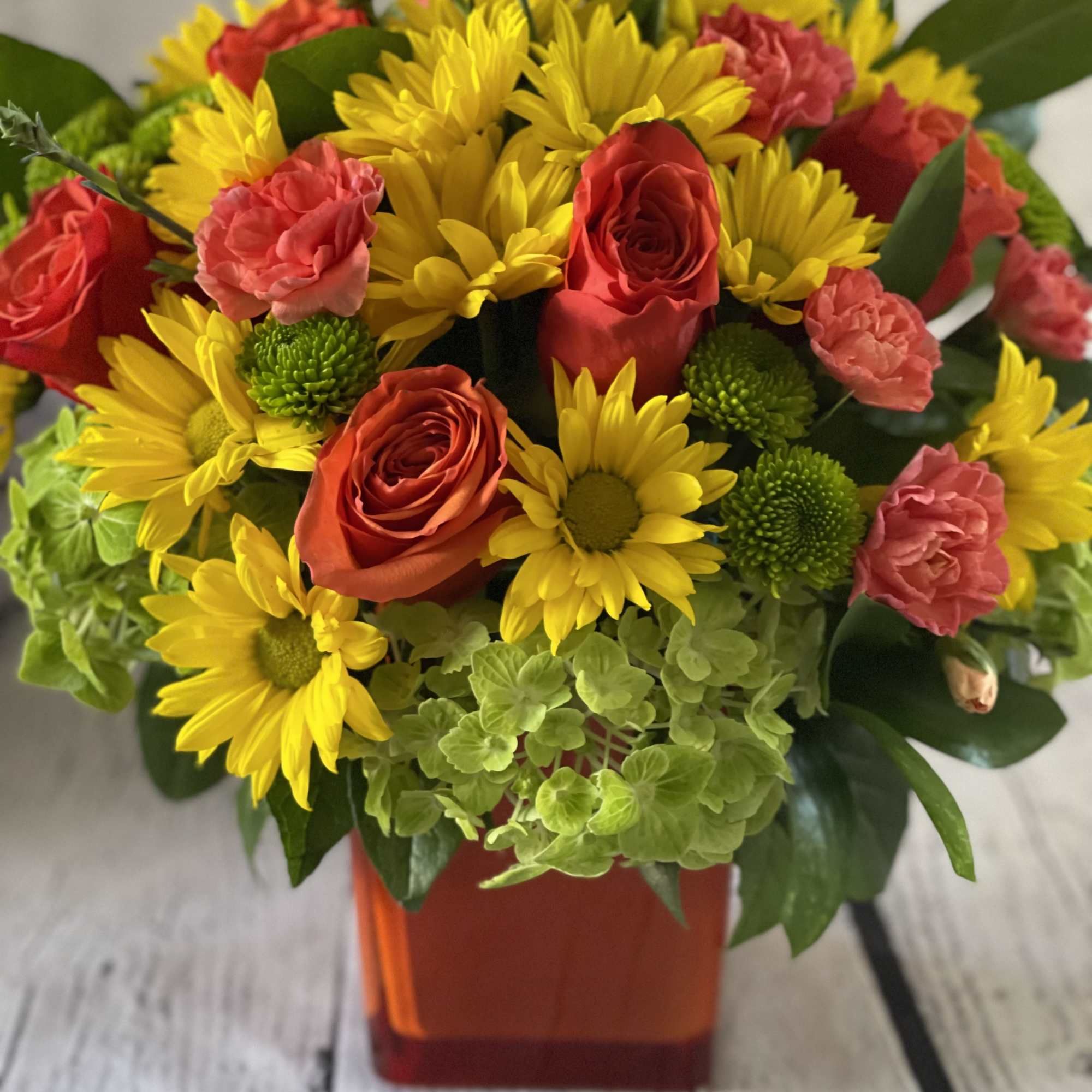 Bouquet of yellow daisies, red roses, and pink carnations in an orange vase
