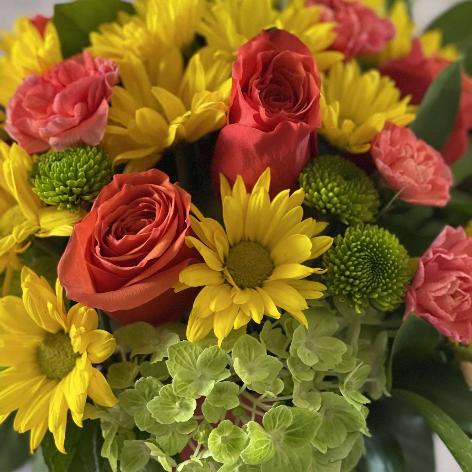 Bouquet of red roses, yellow daisies, and pink carnations in a vase