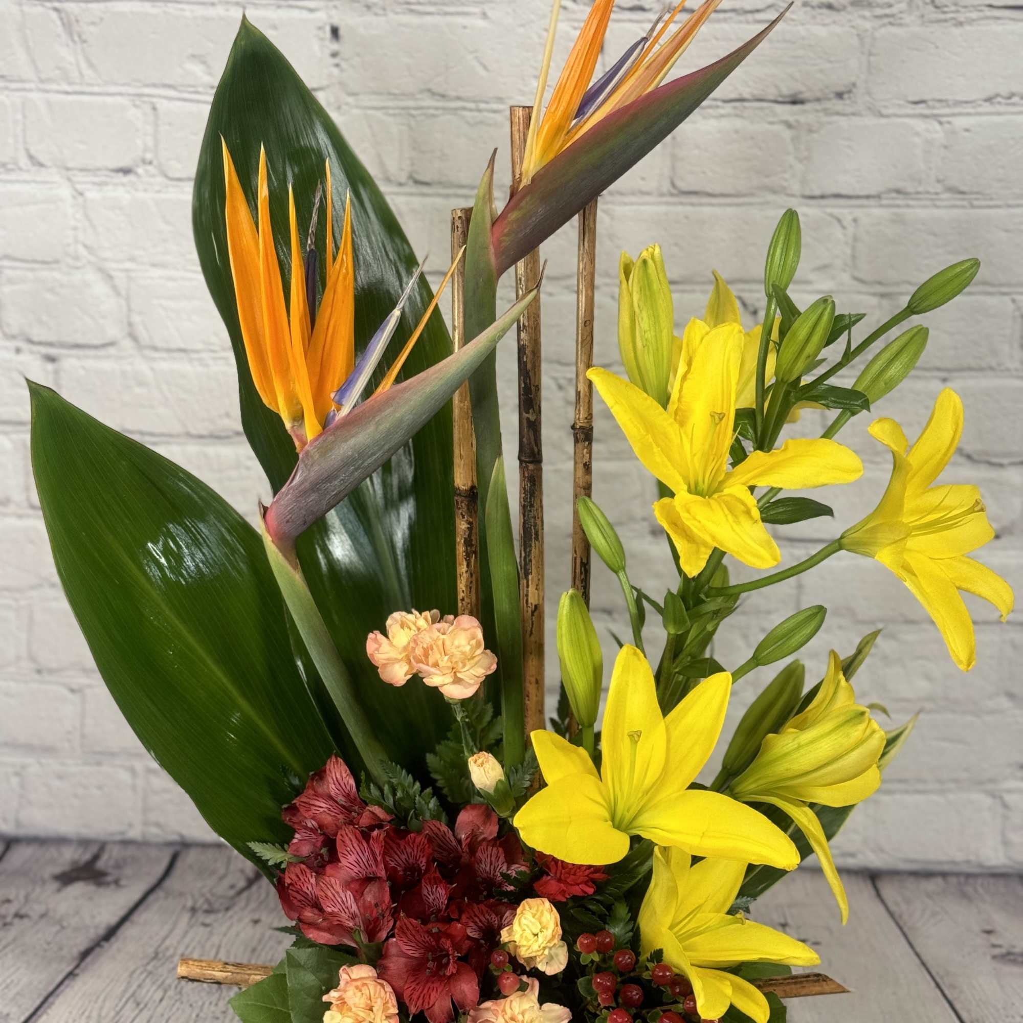 Tropical flower arrangement with yellow lilies and bird of paradise in a black container