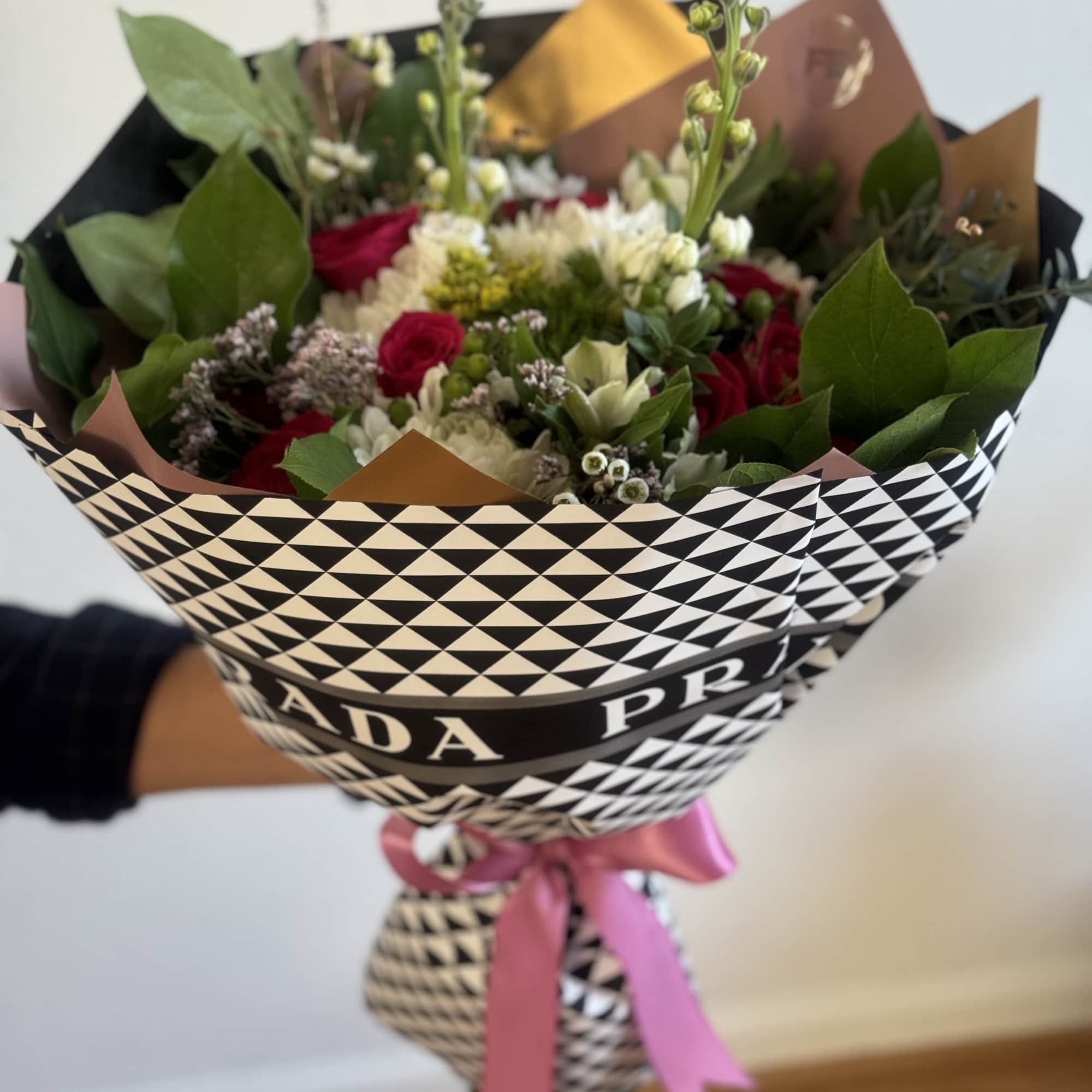 Handheld bouquet of red and white flowers wrapped in patterned paper with a pink ribbon