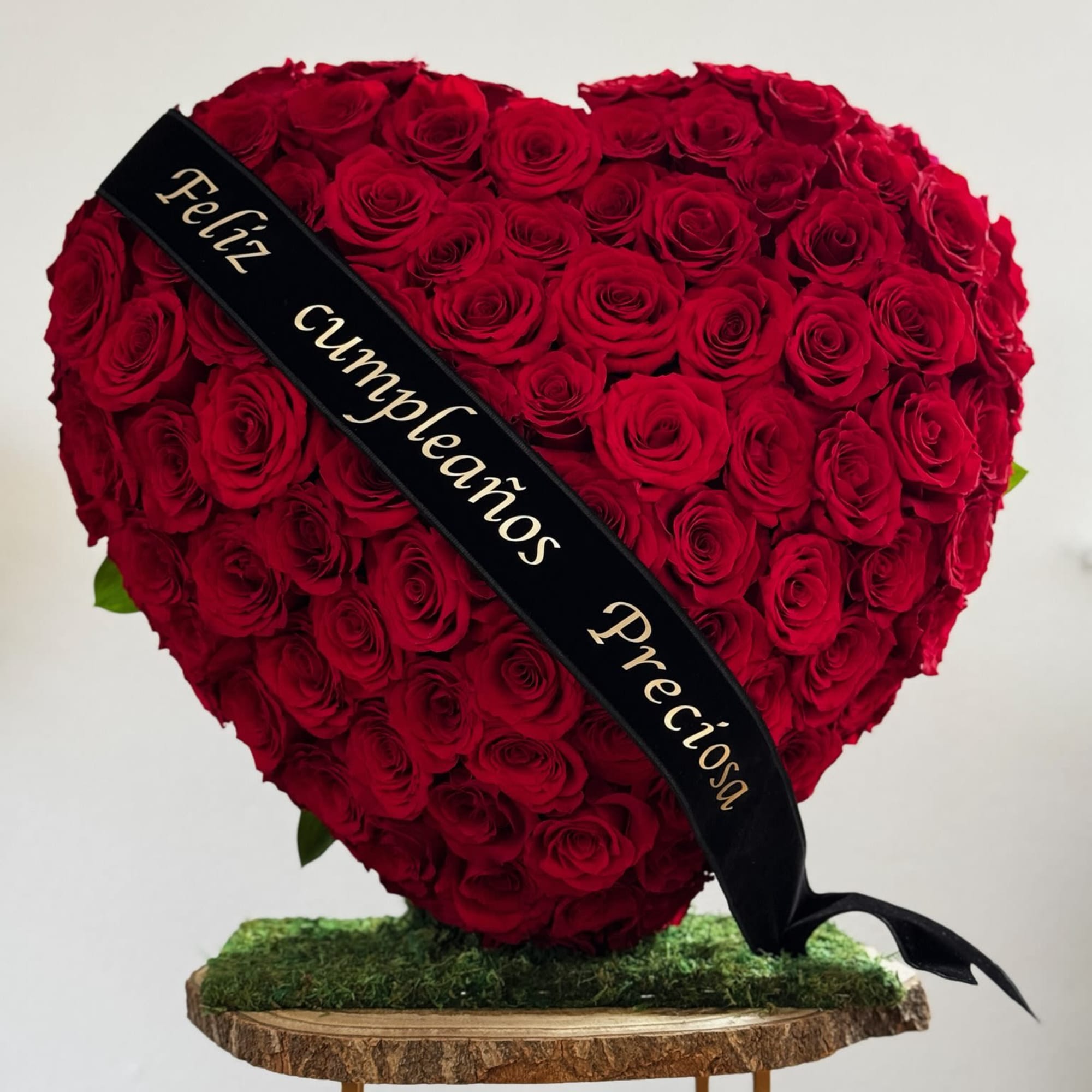 Heart-shaped red rose arrangement with a black ribbon on a wood slab stand