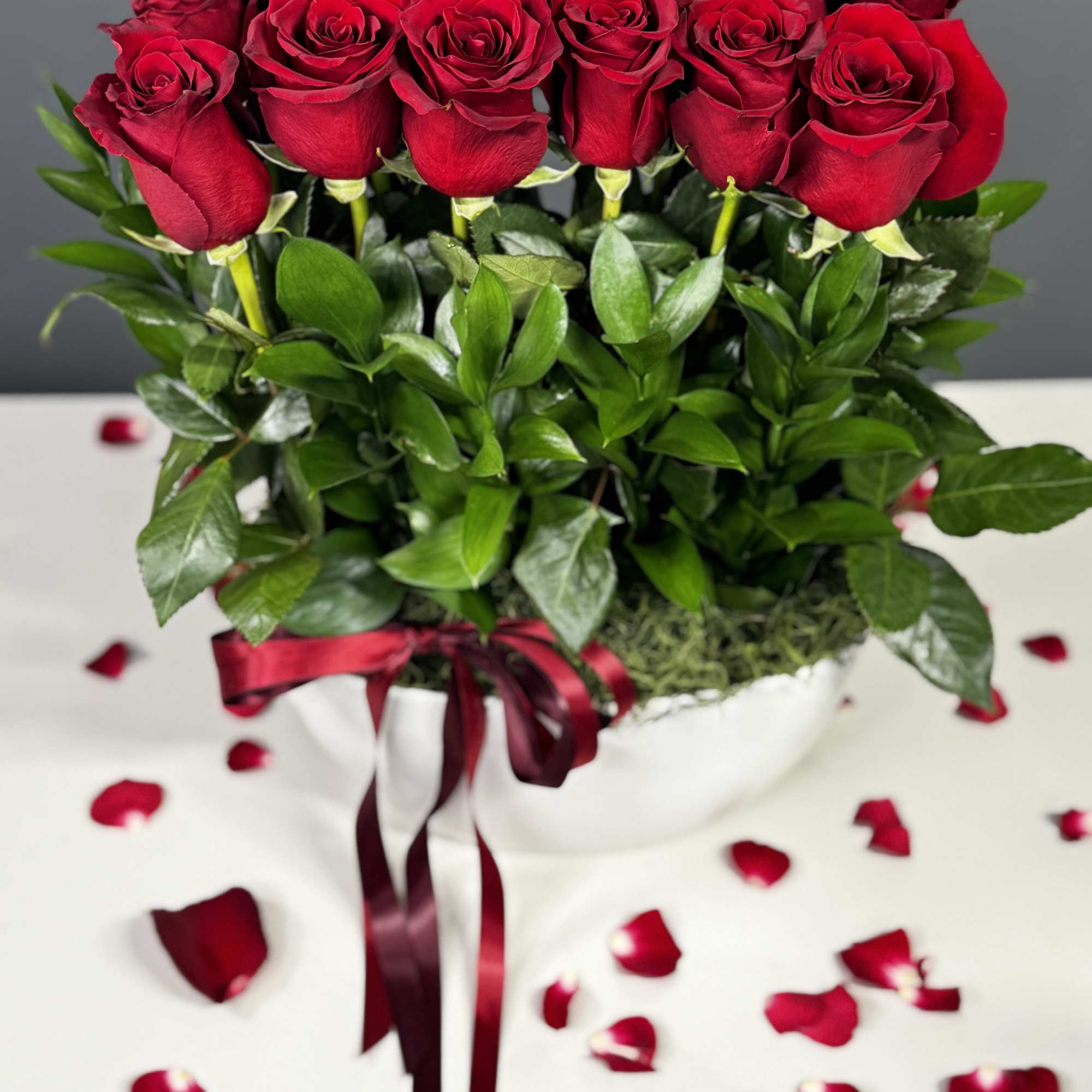 Bouquet of red roses in a white vase with ribbon and scattered petals