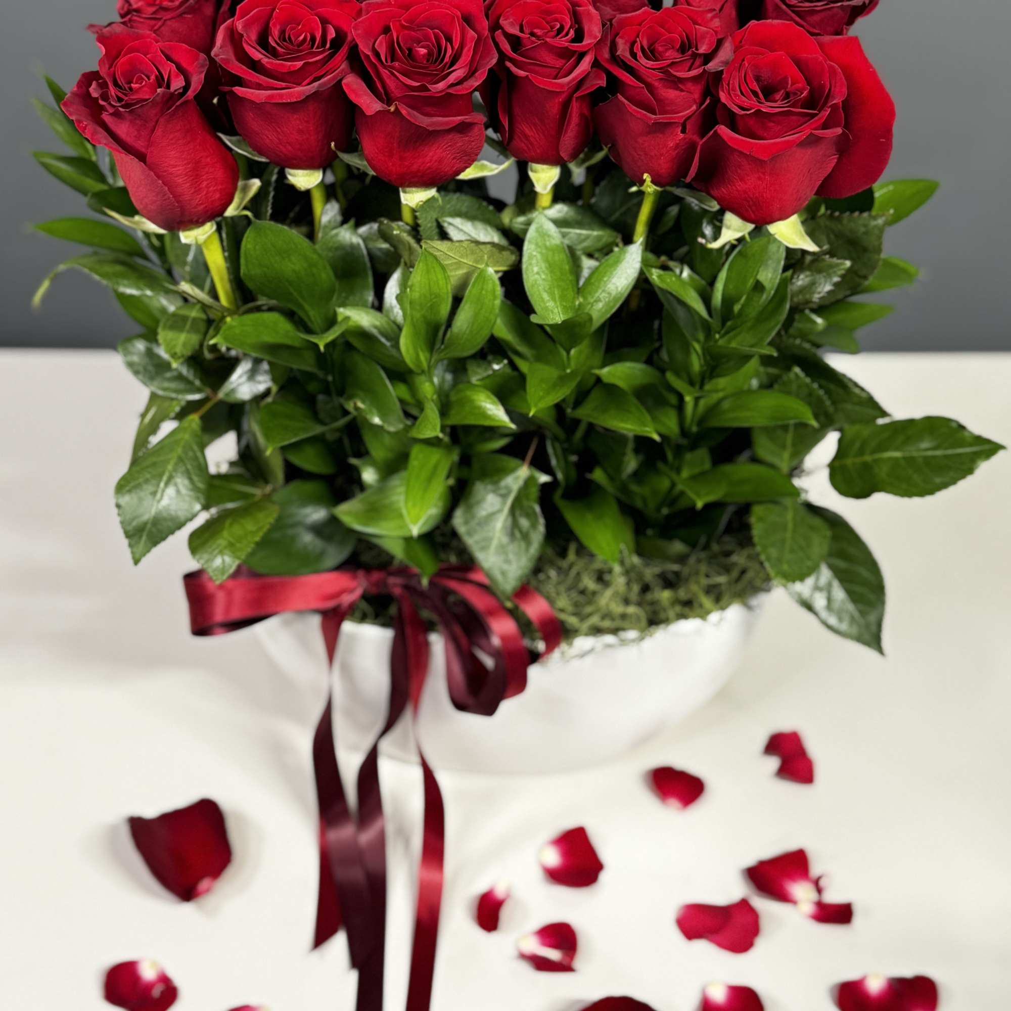 Red roses arranged in a white hatbox with a burgundy ribbon