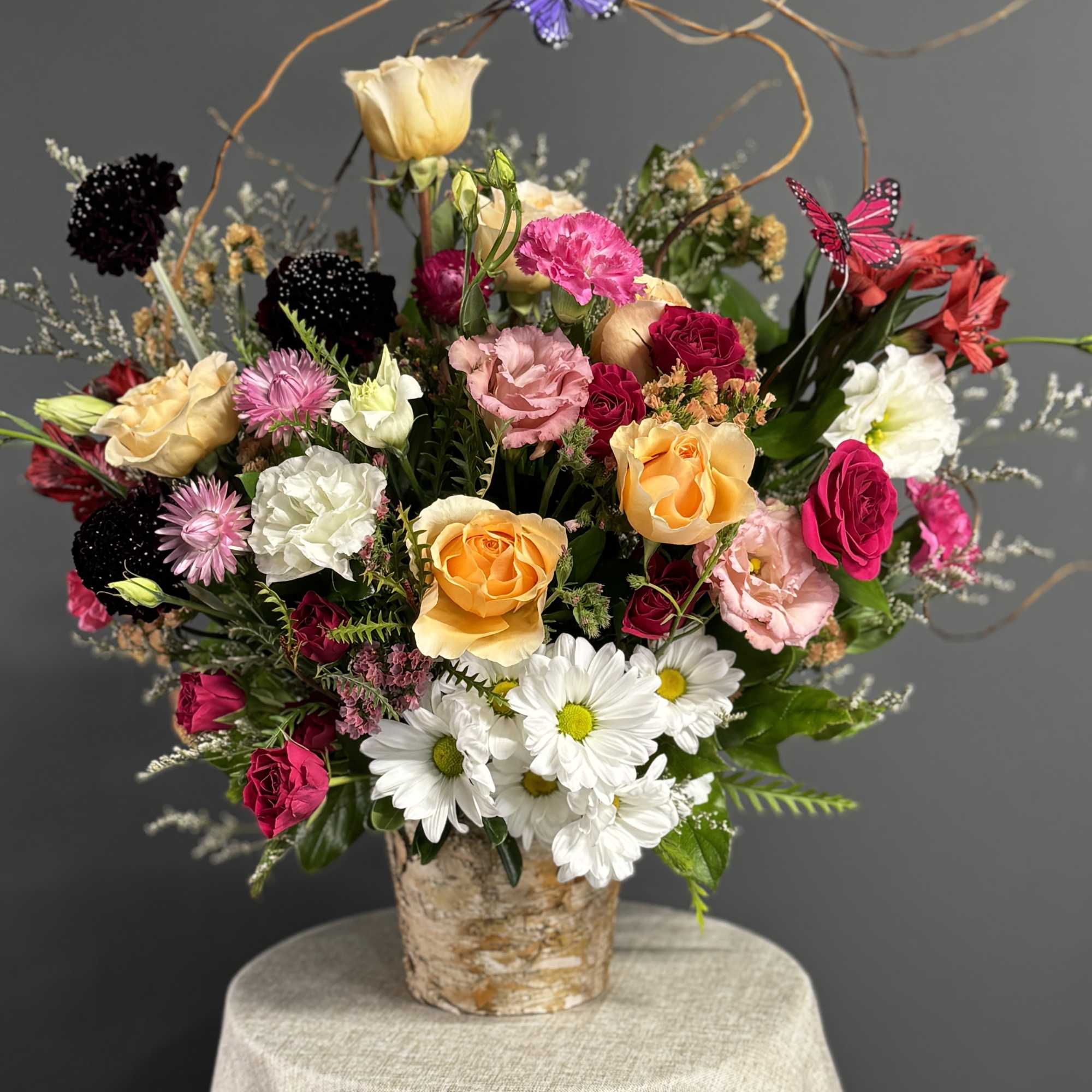 Mixed bouquet of roses, daisies, and carnations in a birch-style container