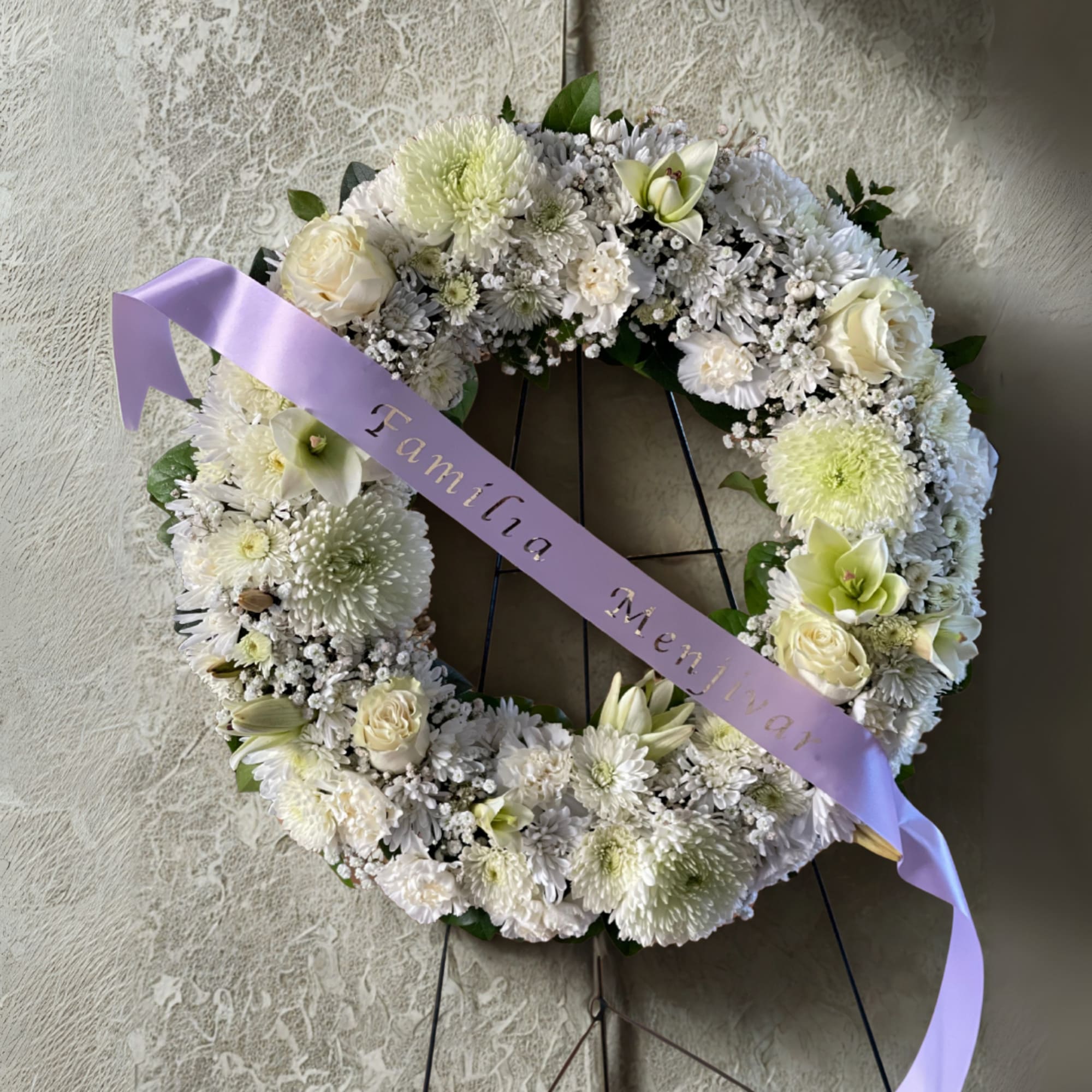 White floral wreath on a stand with a lavender ribbon