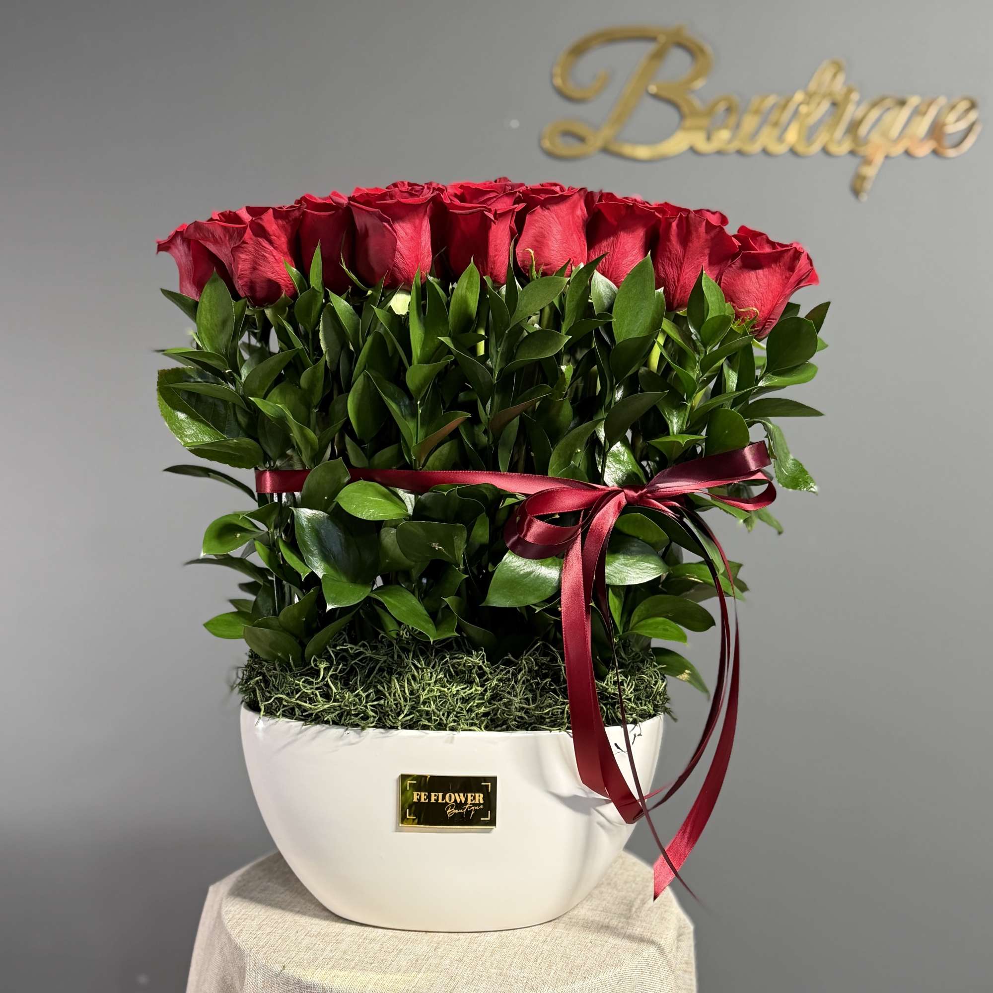 Red roses arranged in a white vase with a burgundy ribbon