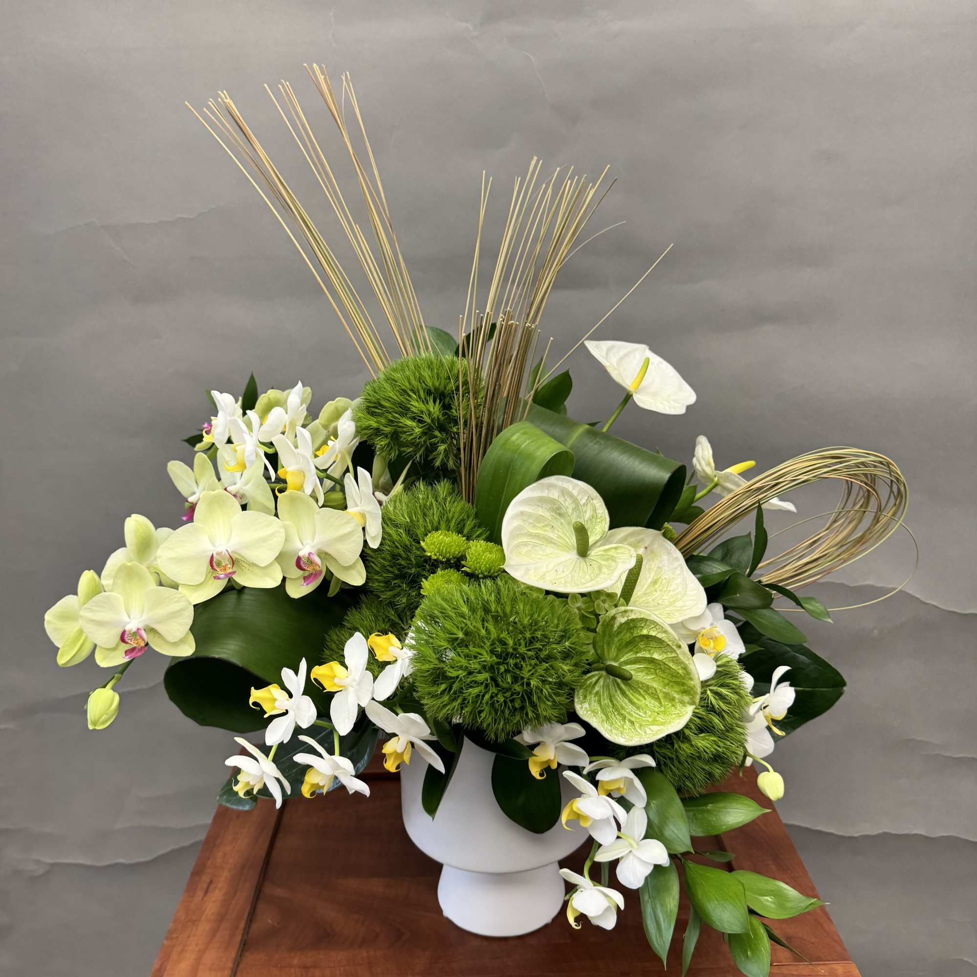 White and green orchid arrangement in a white pedestal vase