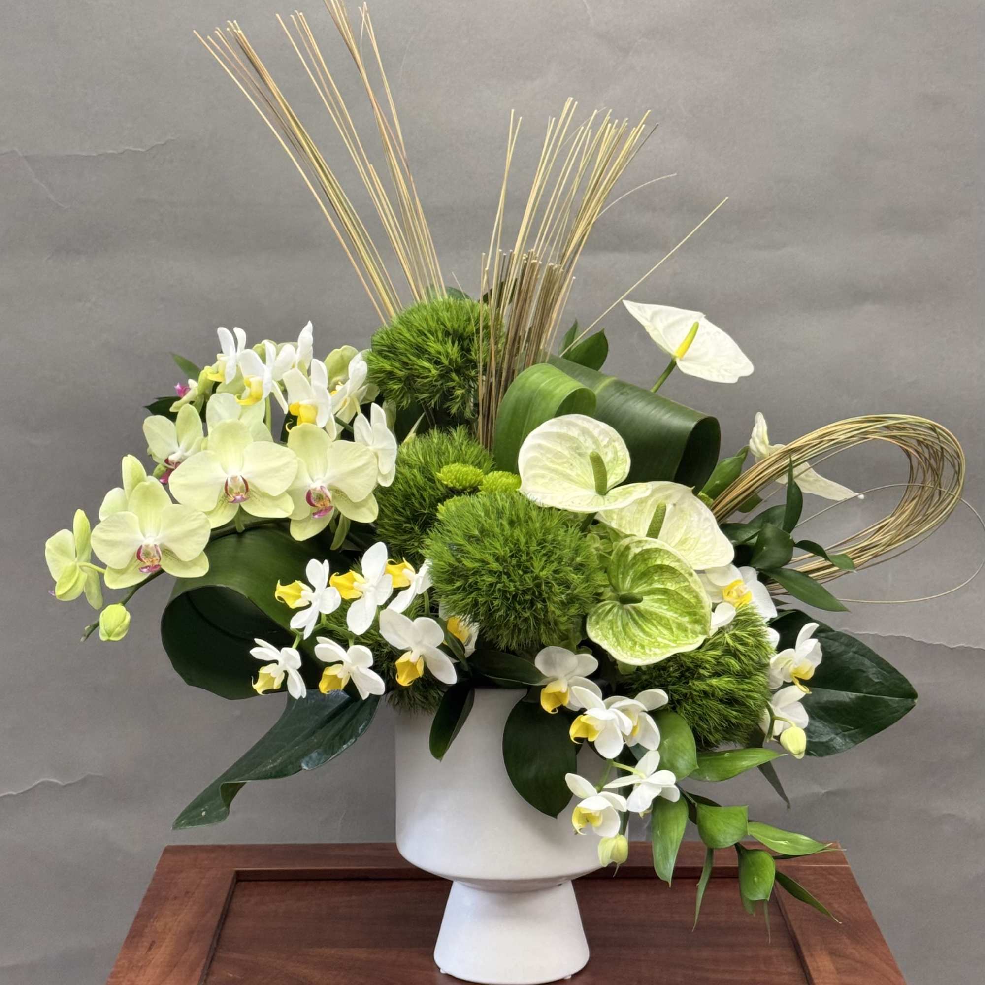White and green floral arrangement in a white pedestal vase