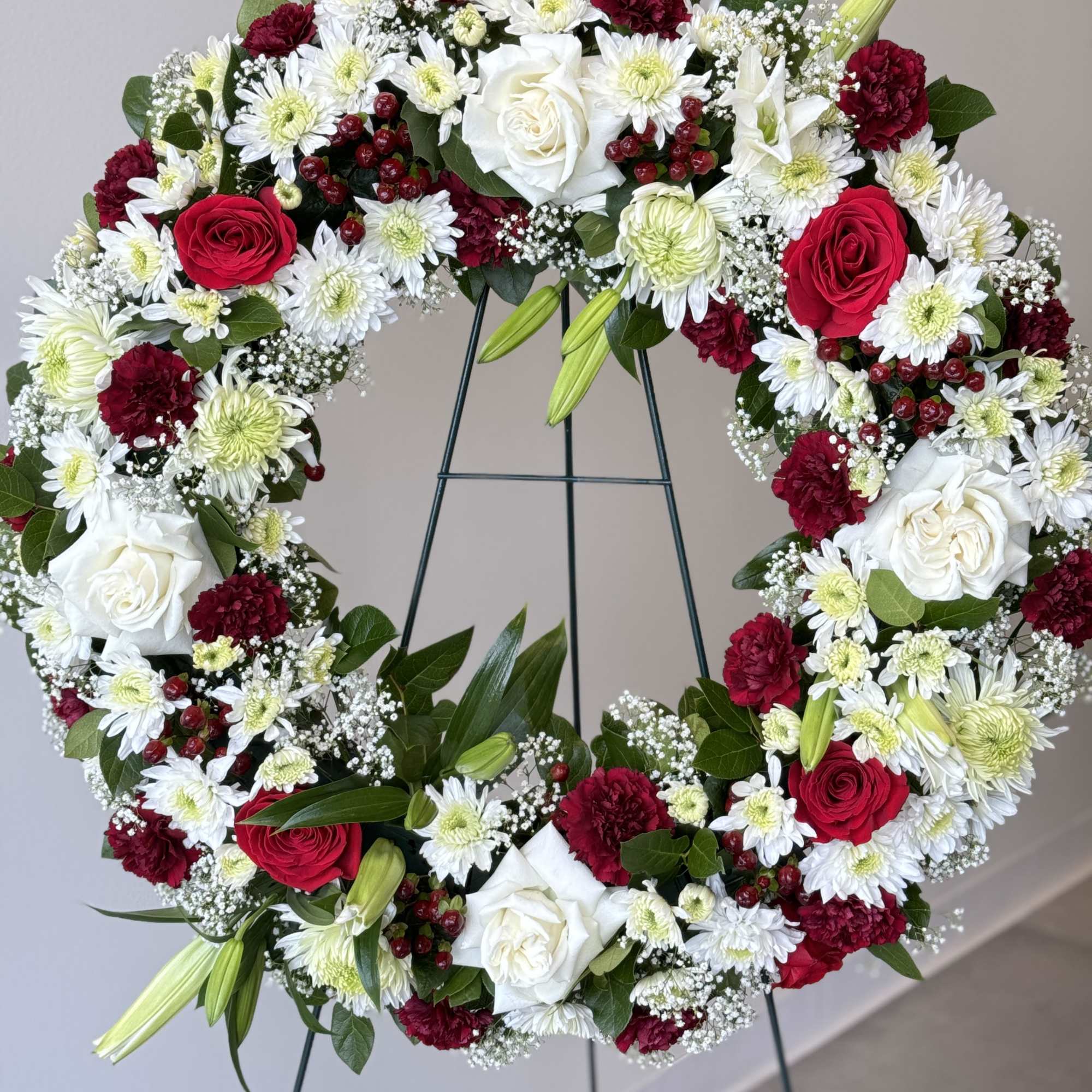 Heart-shaped floral wreath with red, white, and burgundy blooms on a stand
