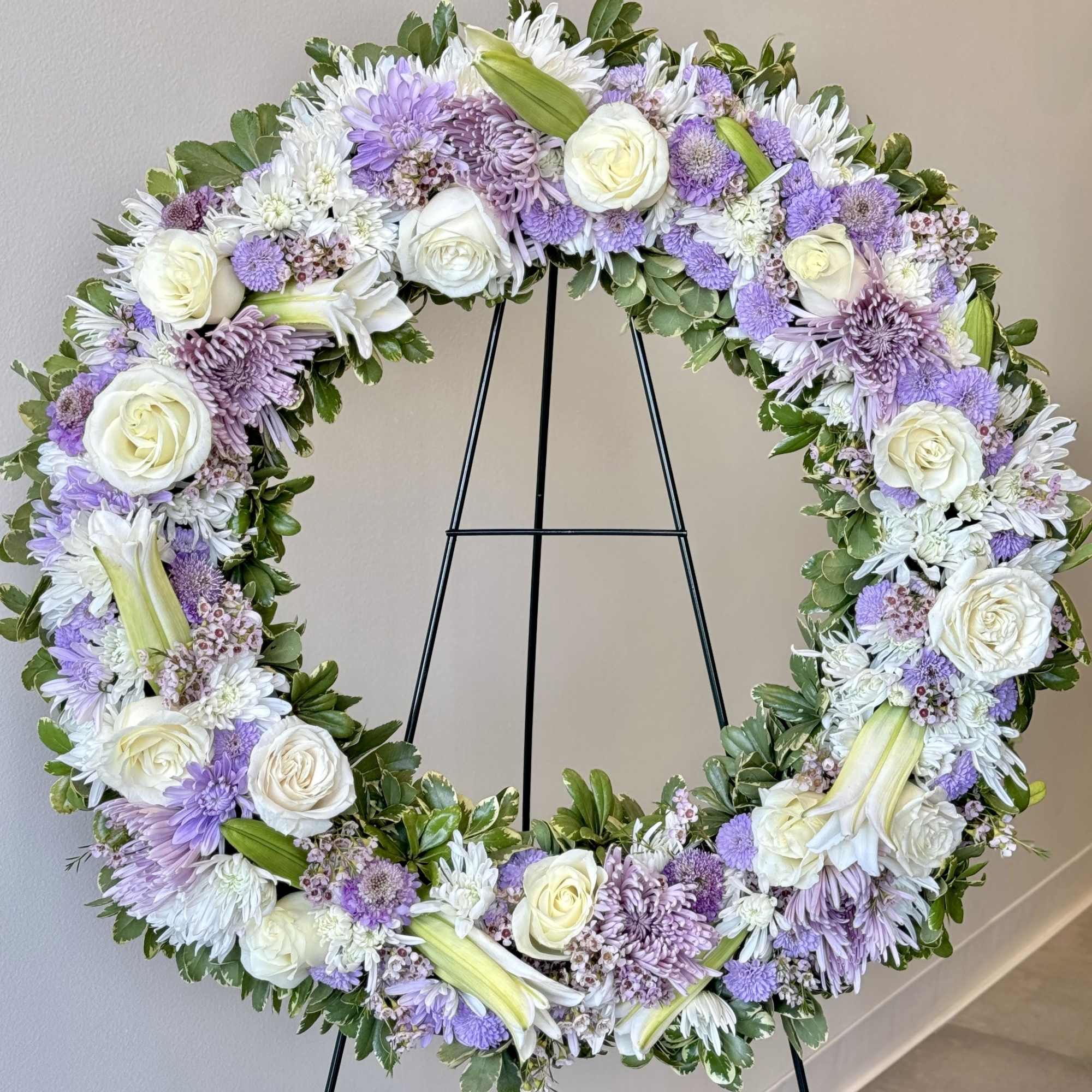 Lavender and white floral wreath on a black stand