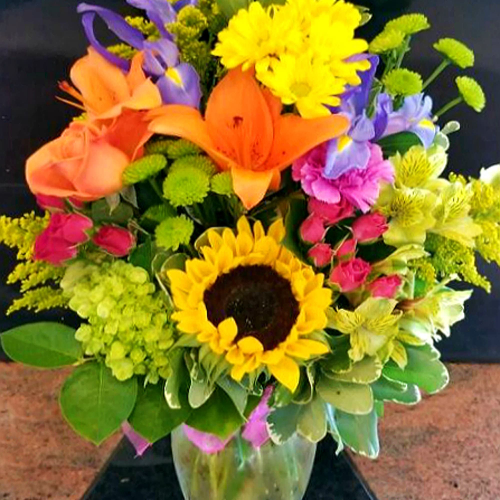 Colorful mixed bouquet with sunflowers, lilies, and chrysanthemums in a glass vase