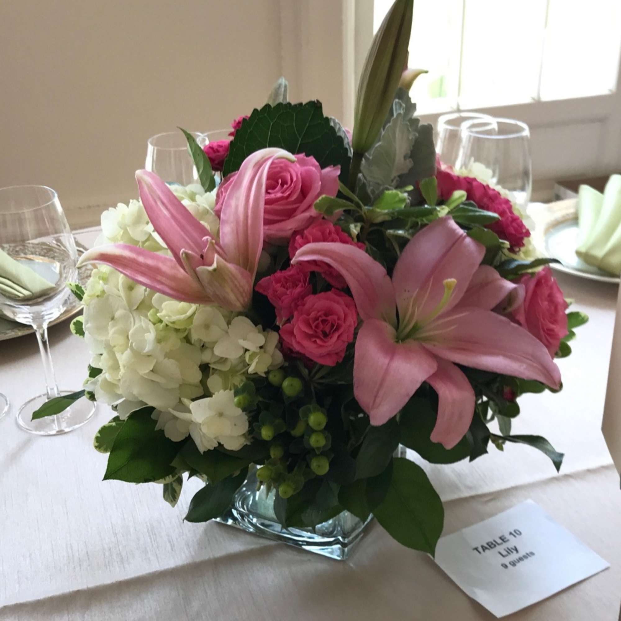 Pink lilies and roses arranged with white hydrangeas in a glass vase