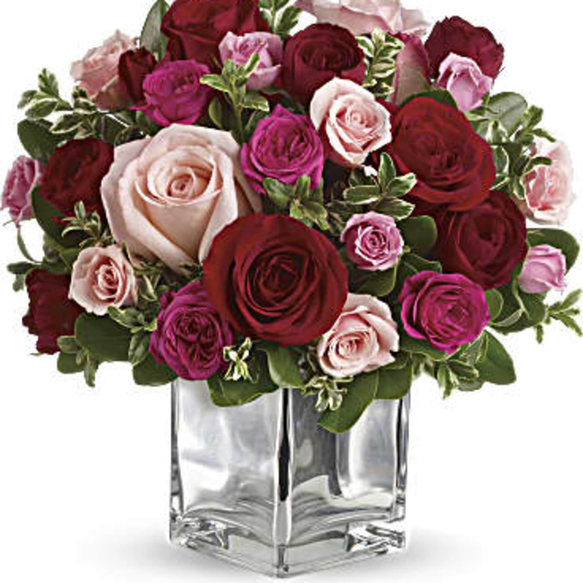 Bouquet of red, pink, and blush roses in a clear glass vase