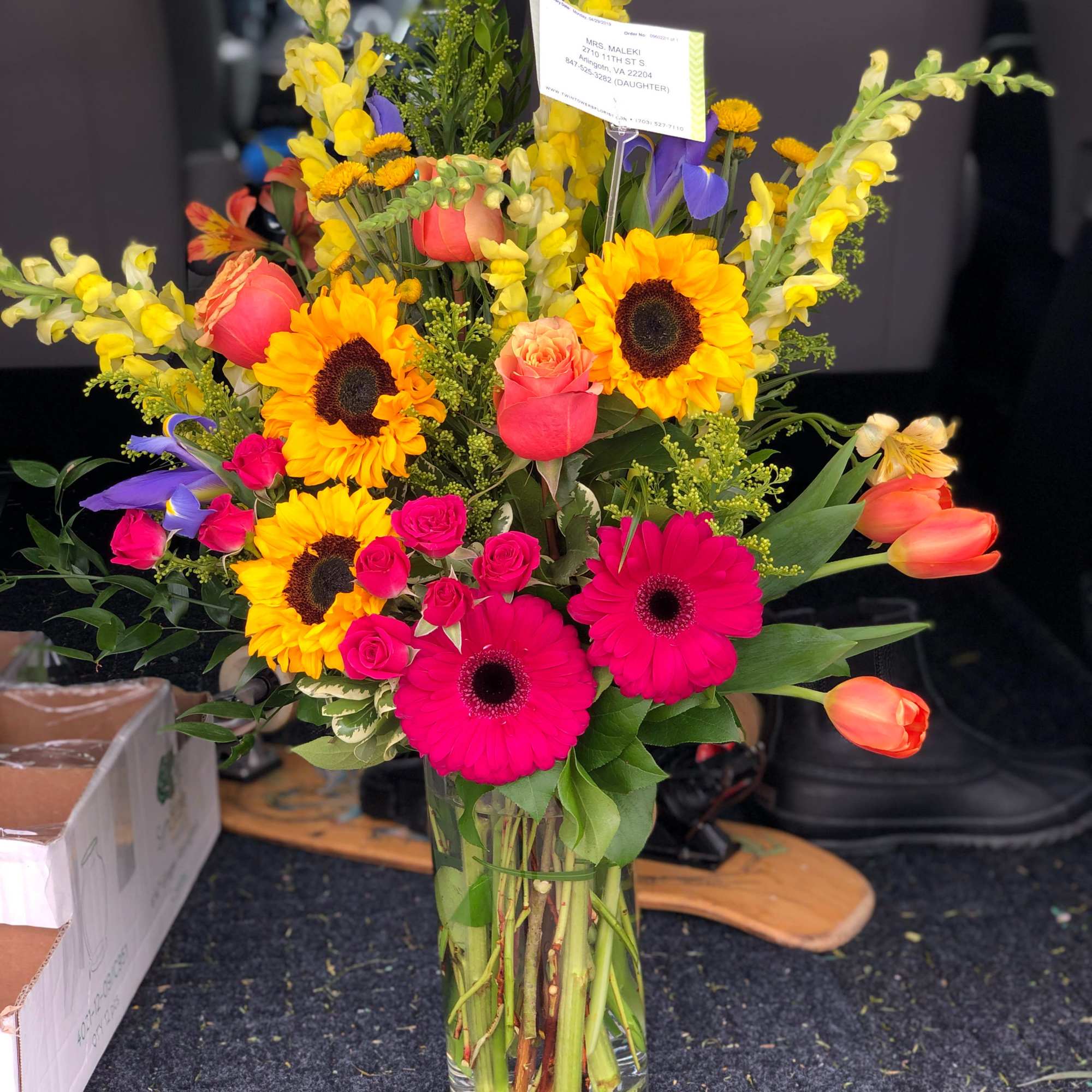 Mixed bouquet in a clear glass vase with sunflowers, roses, gerberas, and tulips